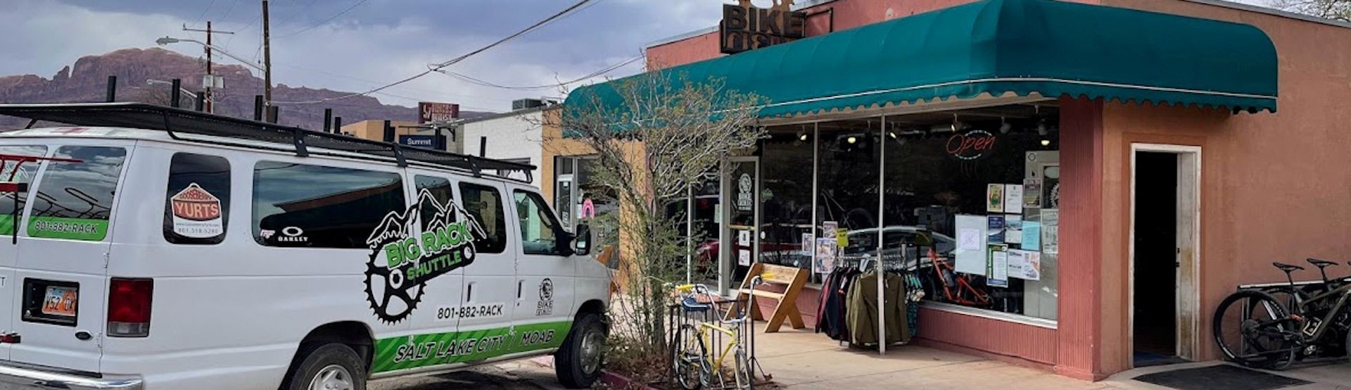 A white van with a bike logo parked next to a bike shop with a green awning.