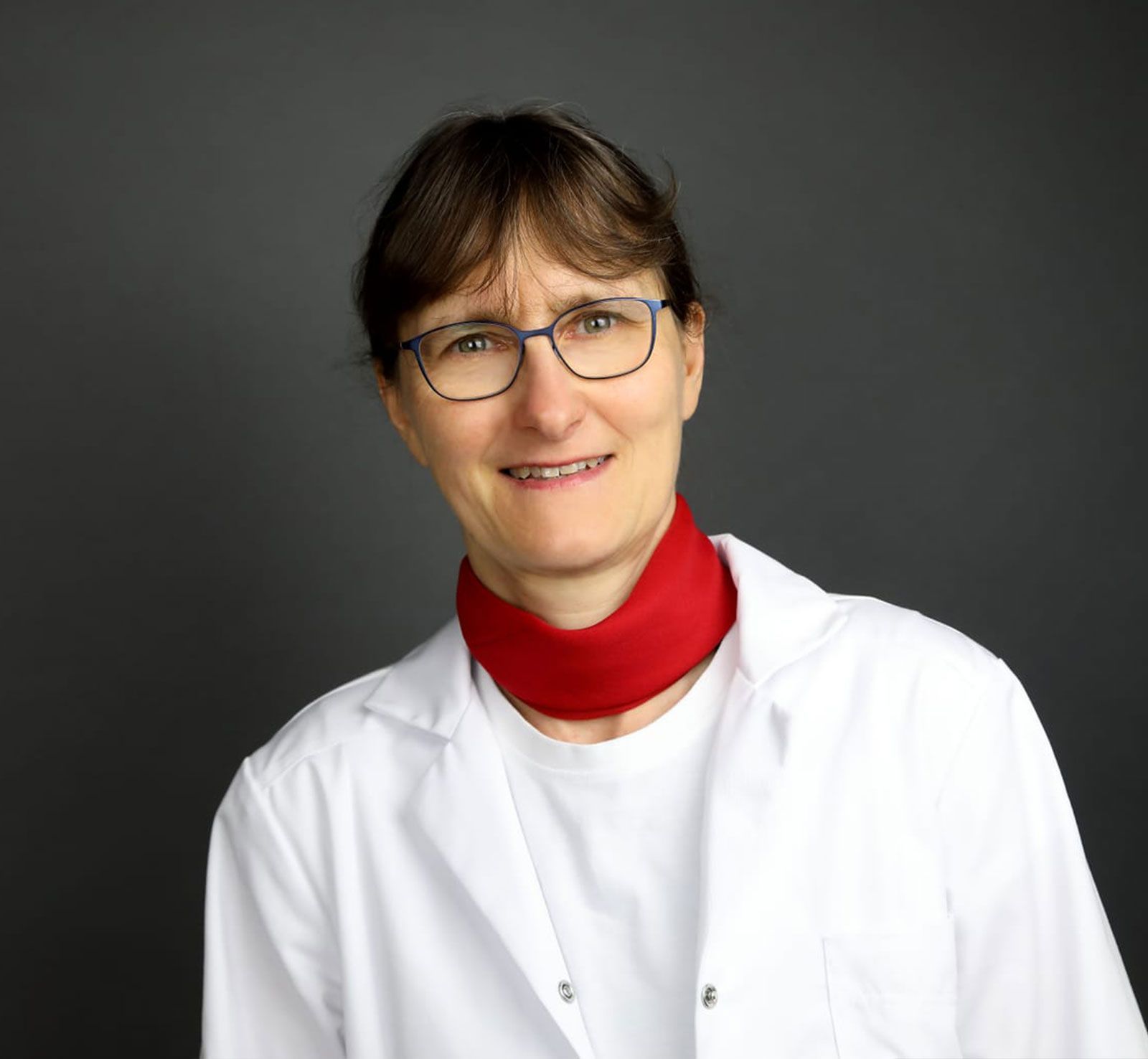 Die Frau trägt eine Brille und einen roten Schal um den Hals.