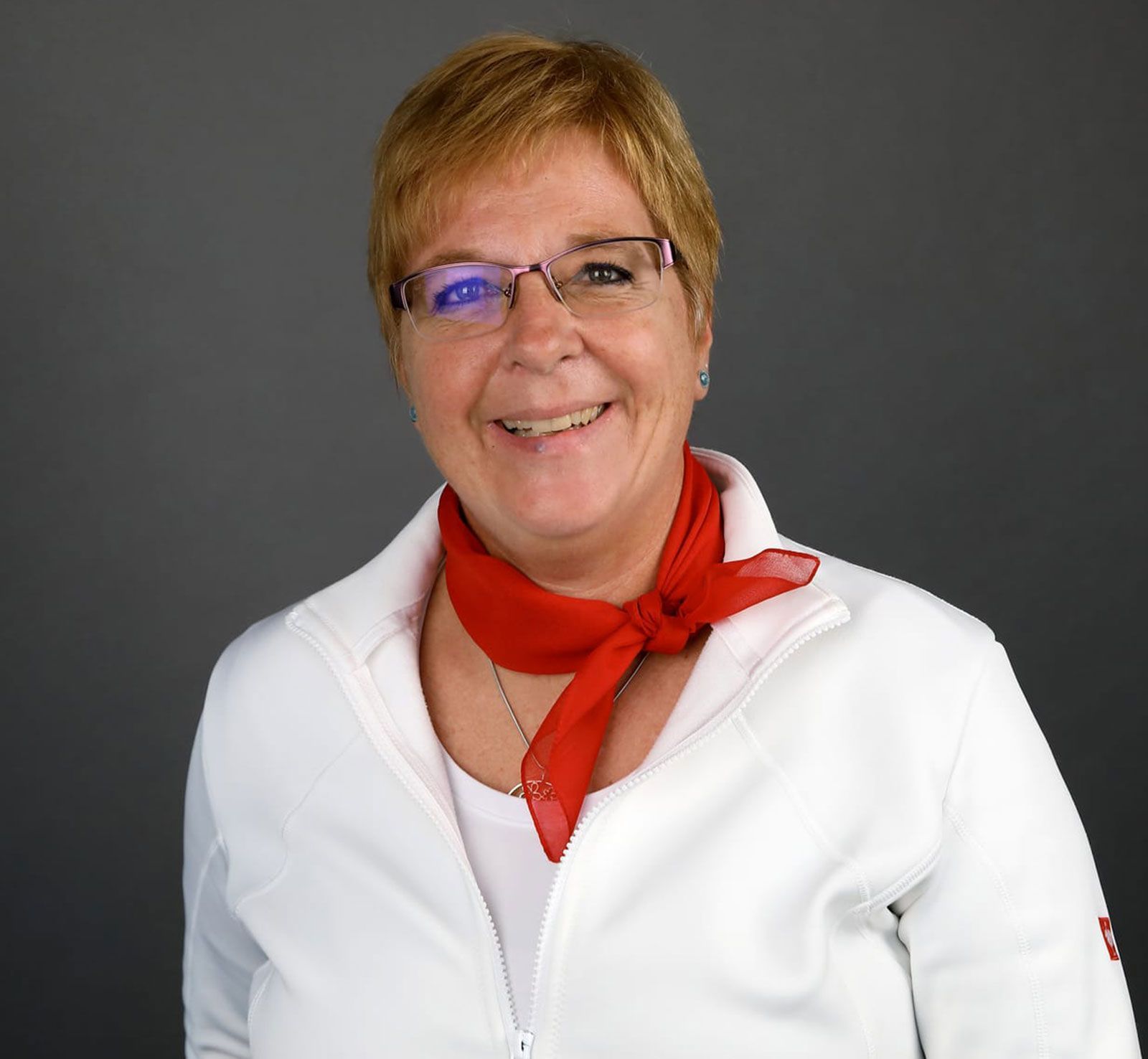 Eine Frau mit Brille und rotem Schal lächelt in die Kamera.