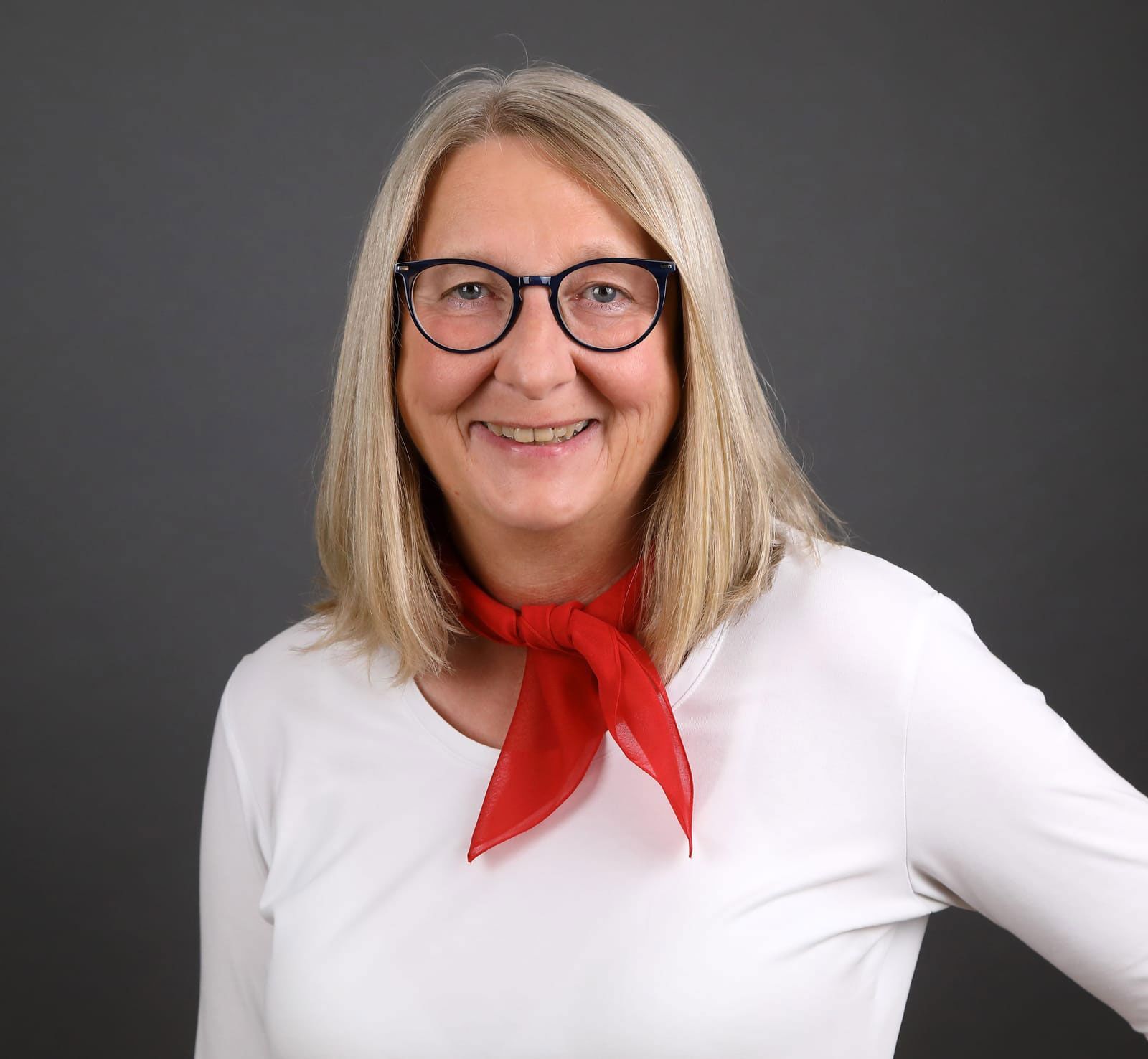 Eine Frau mit Brille und rotem Schal lächelt in die Kamera.