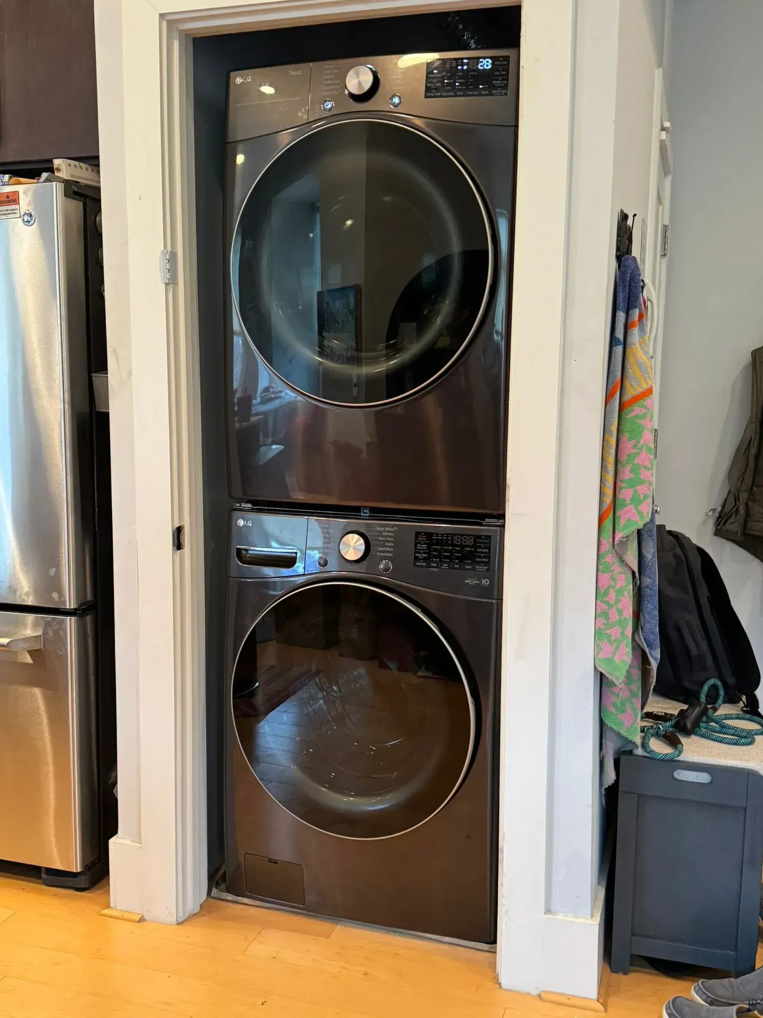 Stacked washer and dryer in a closet with white trim and a laundry hamper beside them