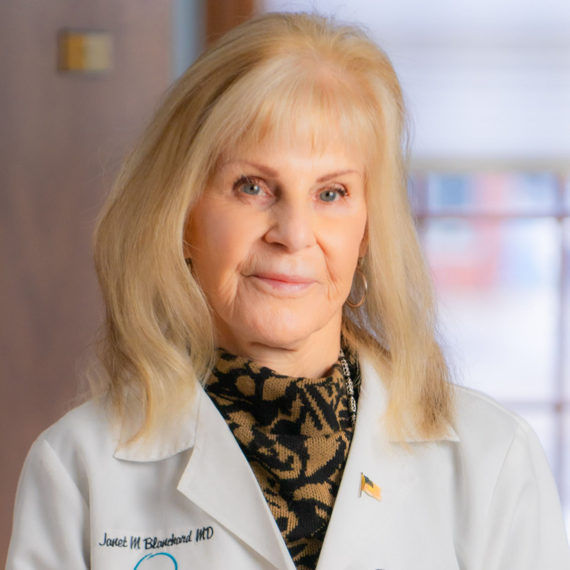 Woman in white lab coat smiles. Her name tag reads 