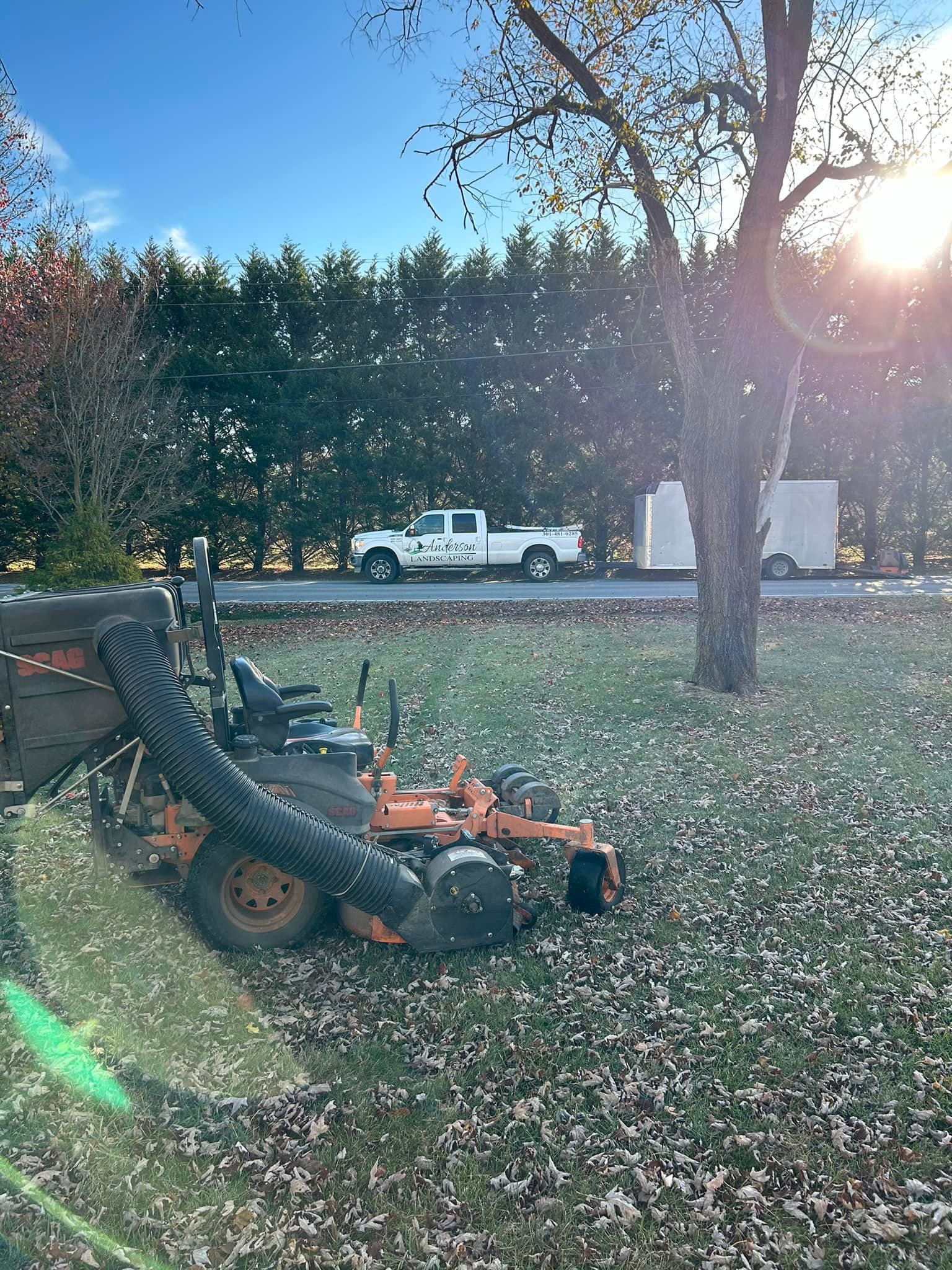 A lawn mower with a vacuum attached to it is sitting in a field of leaves.