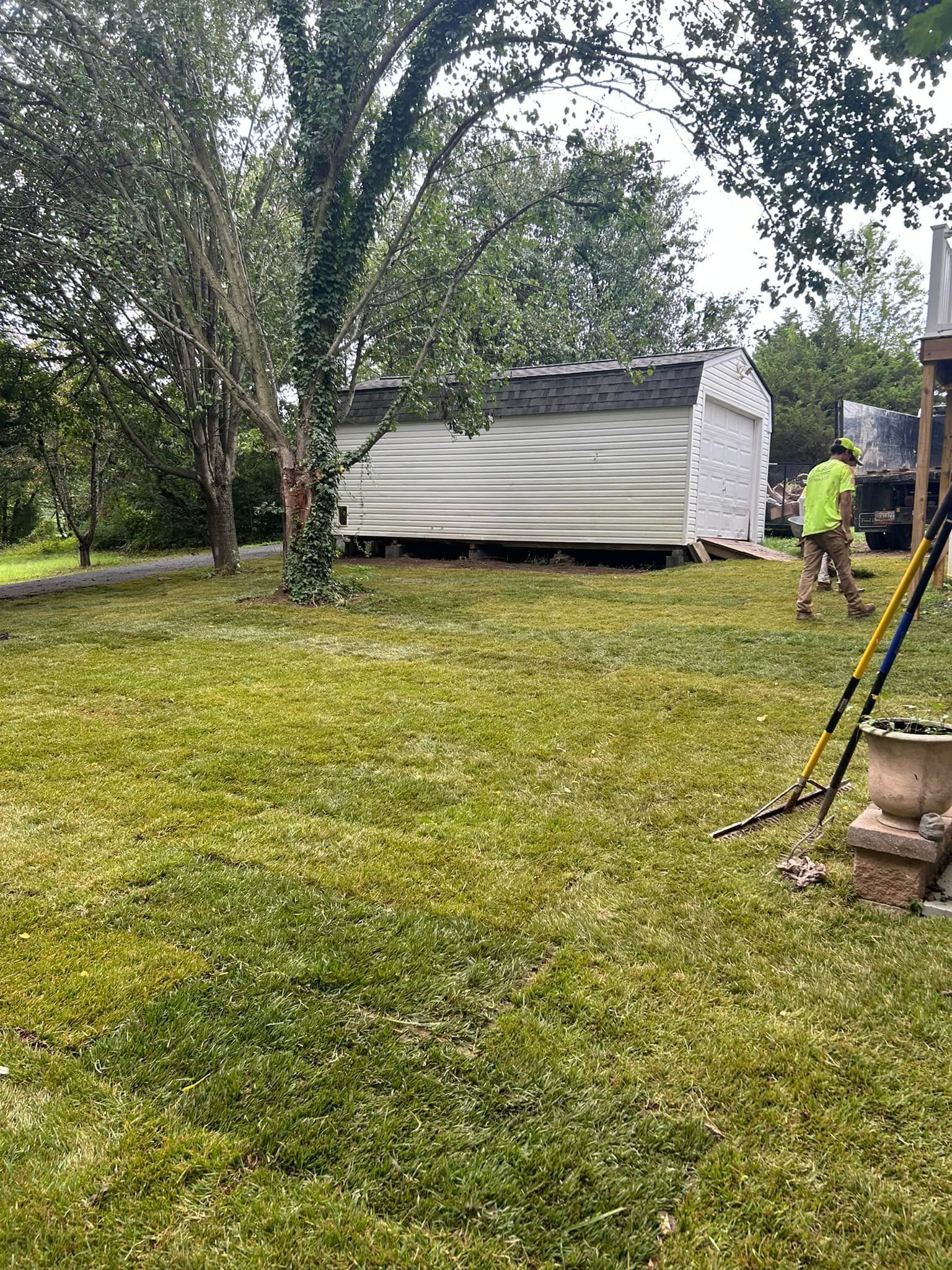 A man is mowing the grass in a yard in front of a shed.