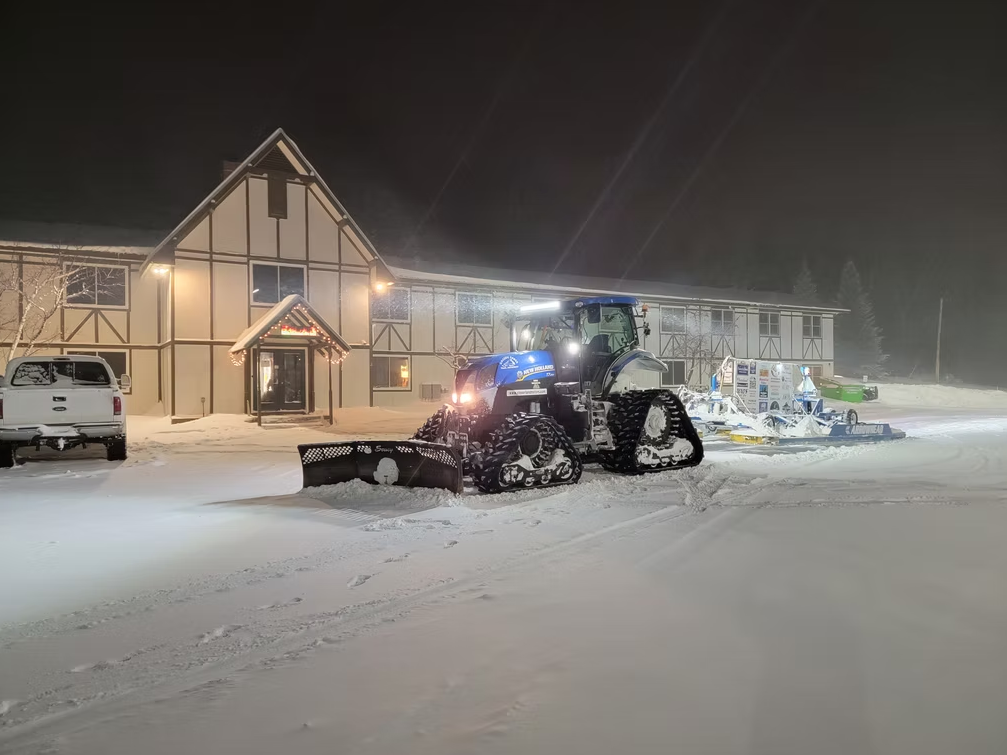Snowplow clearing a snowy driveway outside a lit house at night