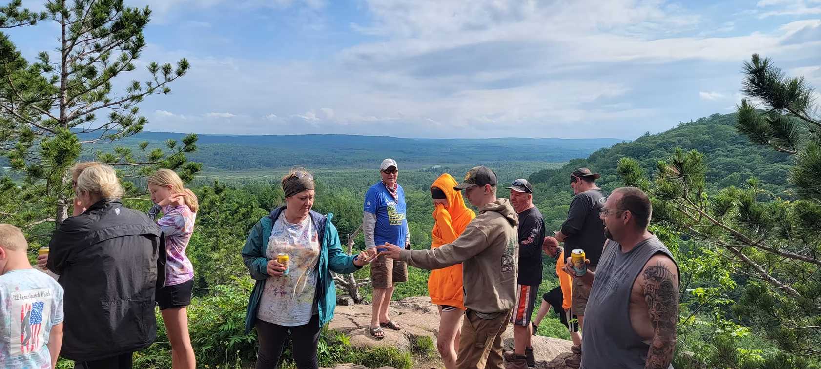 Group of people standing on a hilltop overlooking a scenic green valley under a blue sky