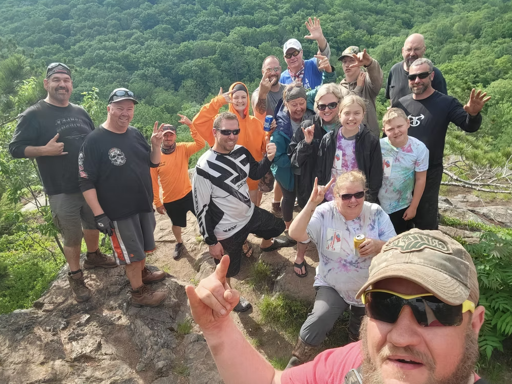 Group of hikers posing on a rocky trail with green trees in the background.