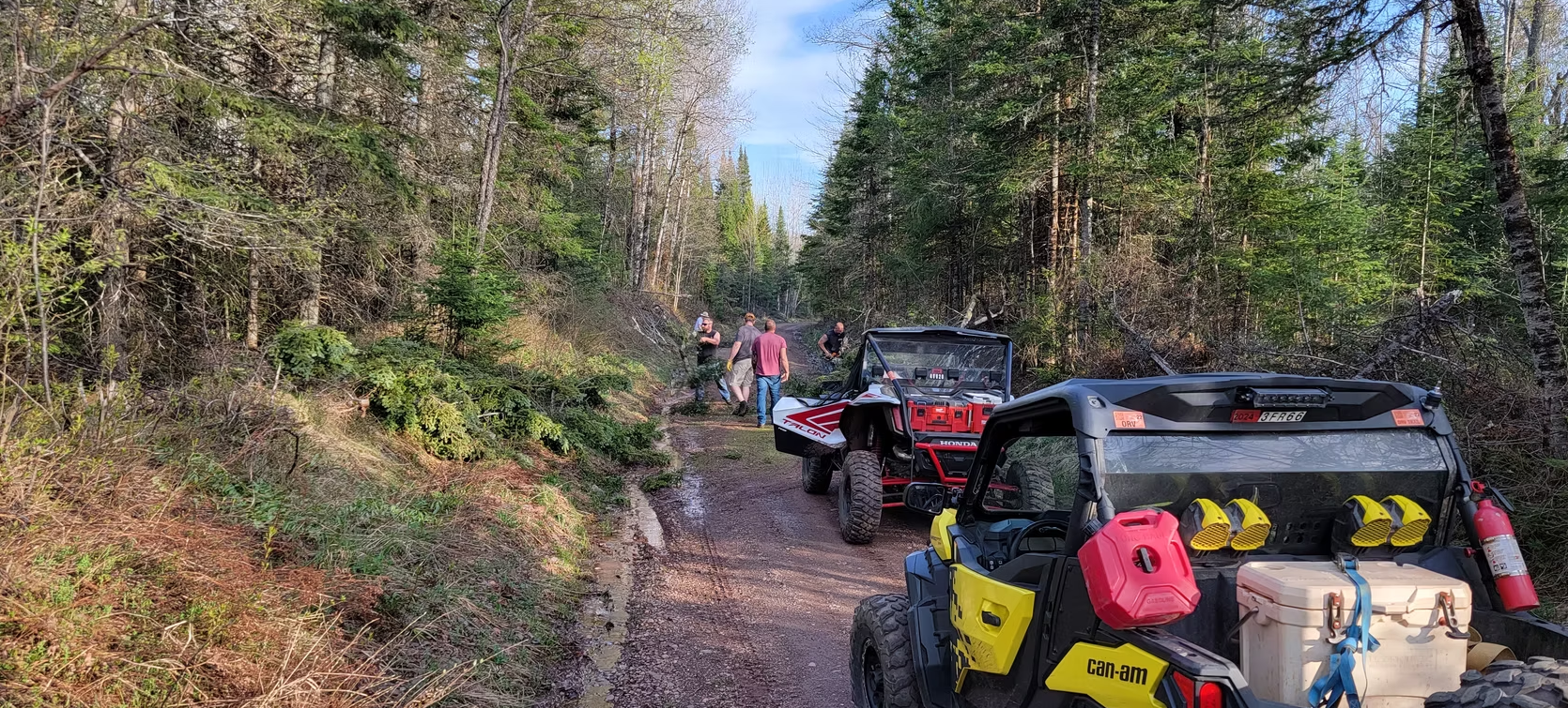 Off-road vehicles lined up on a muddy forest trail, with gear strapped to the rear vehicle.