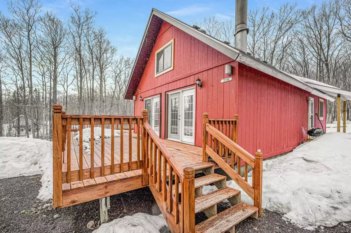 Red cabin with snowy yard and wooden deck stairs in a winter forest