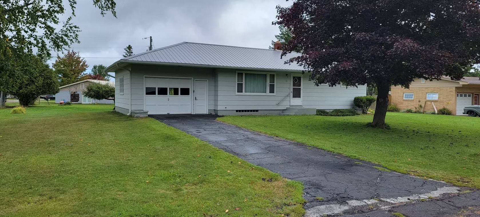Single-story white house with attached garage, grassy front yard, and dark driveway under overcast sky