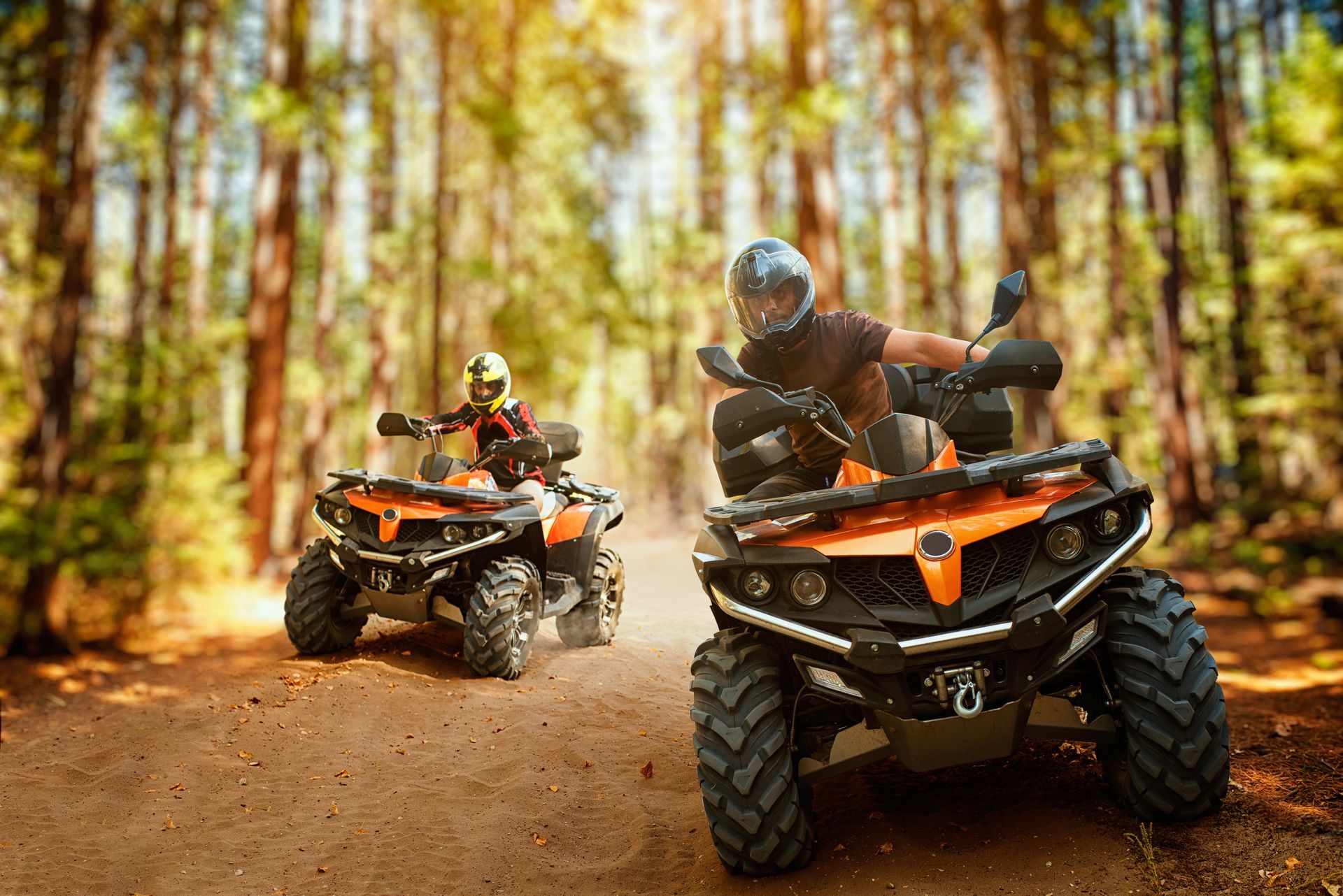 Two ATVs racing on a dirt trail in a forest, kicking up dust.