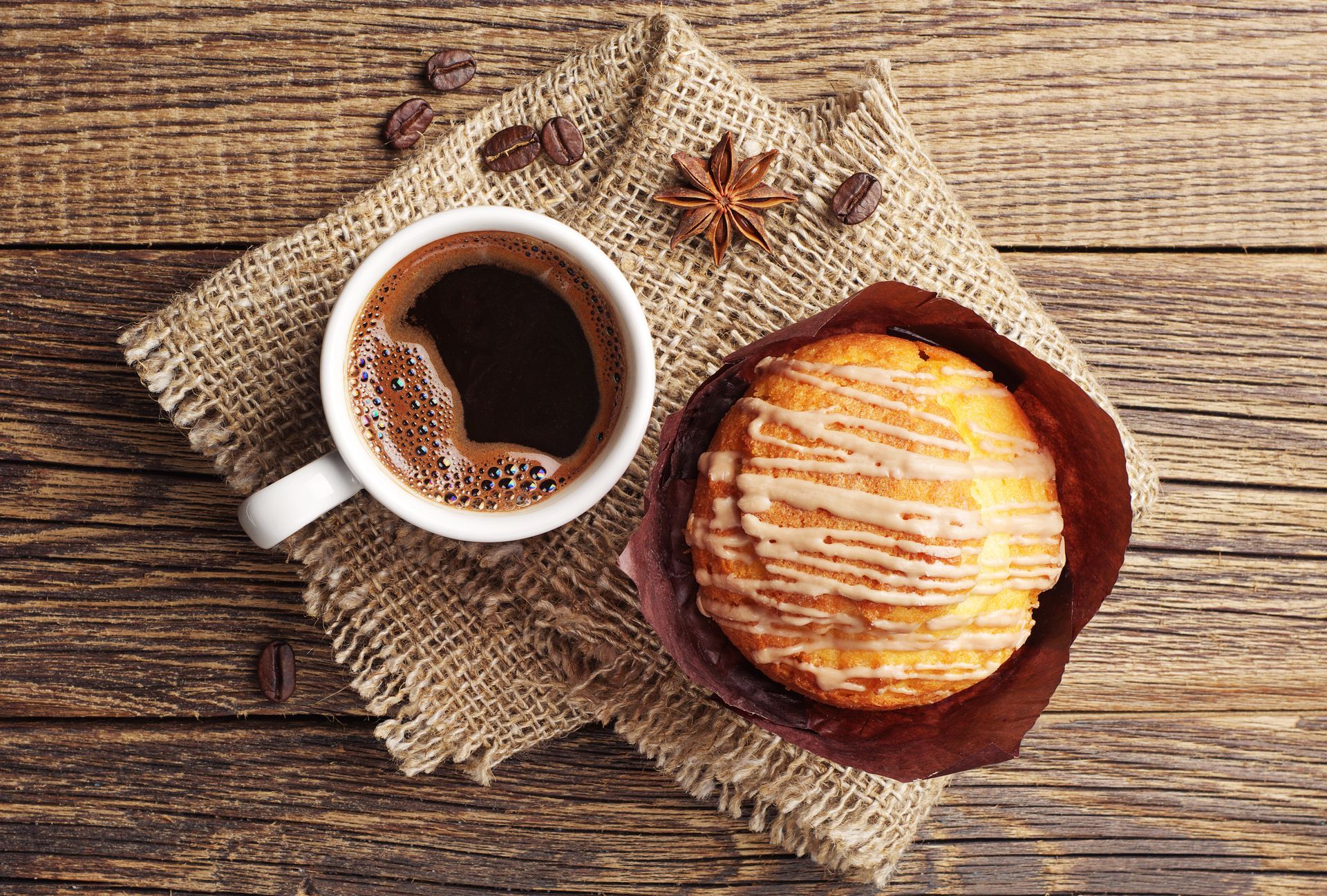 Coffee and a pastry on burlap cloth with a star anise on a rustic wooden table