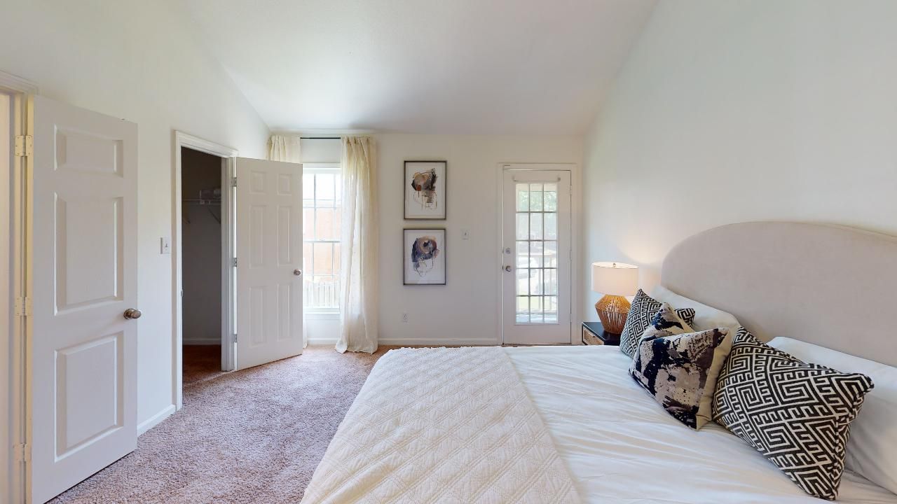 Bedroom with bed, doorway, open door to outdoors, artwork, and curtains.