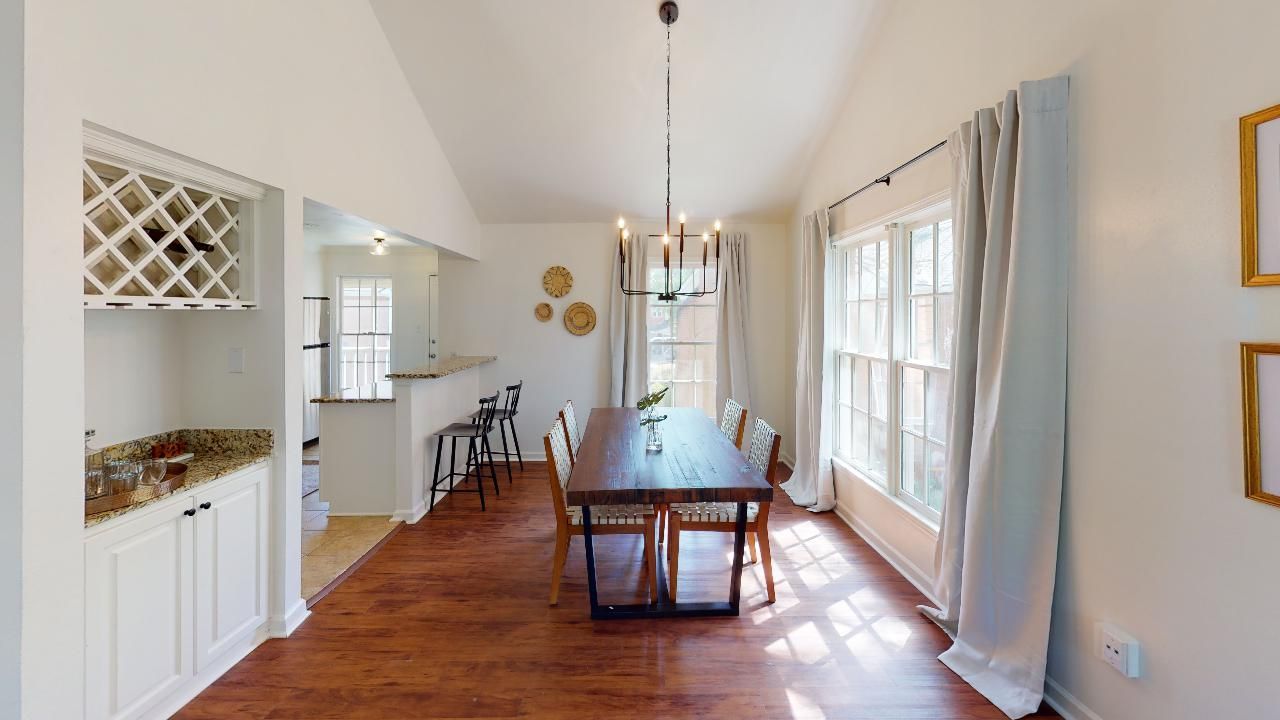 Dining room with a long wooden table, built-in wine rack, and large windows with gray curtains.