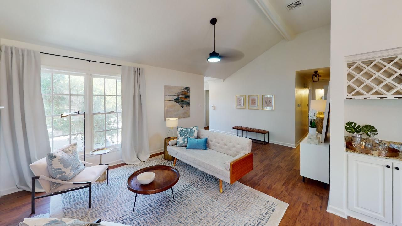 Living room with white walls, a sofa, and large windows. Brown coffee table on a patterned rug.