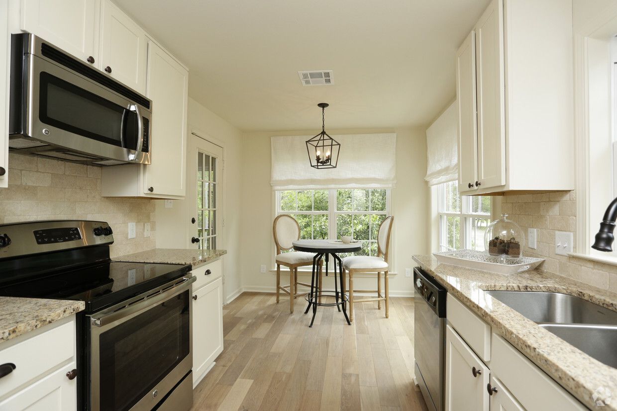 A small kitchen with light cabinets, stainless steel appliances, and a small table by a window.