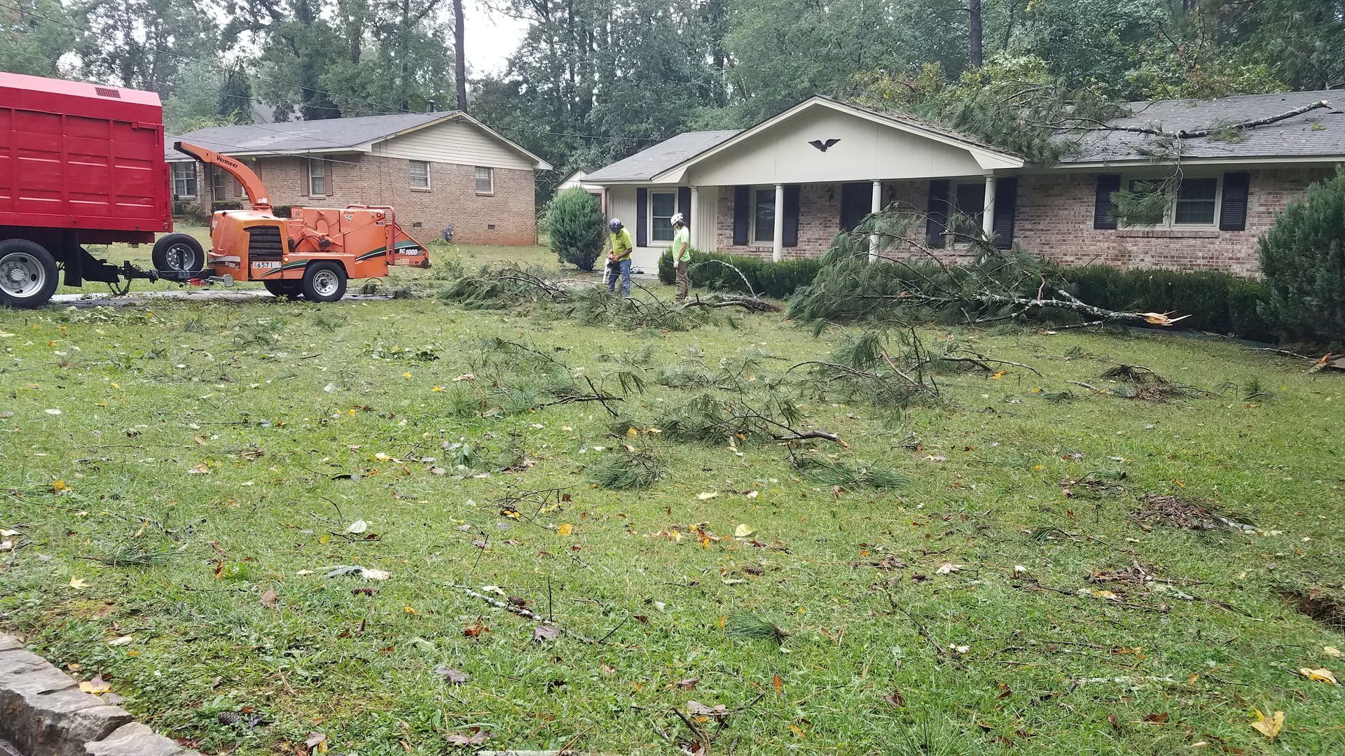 Storm cleanup crew removes large fallen branches from a residential property and  installs tarp on roof