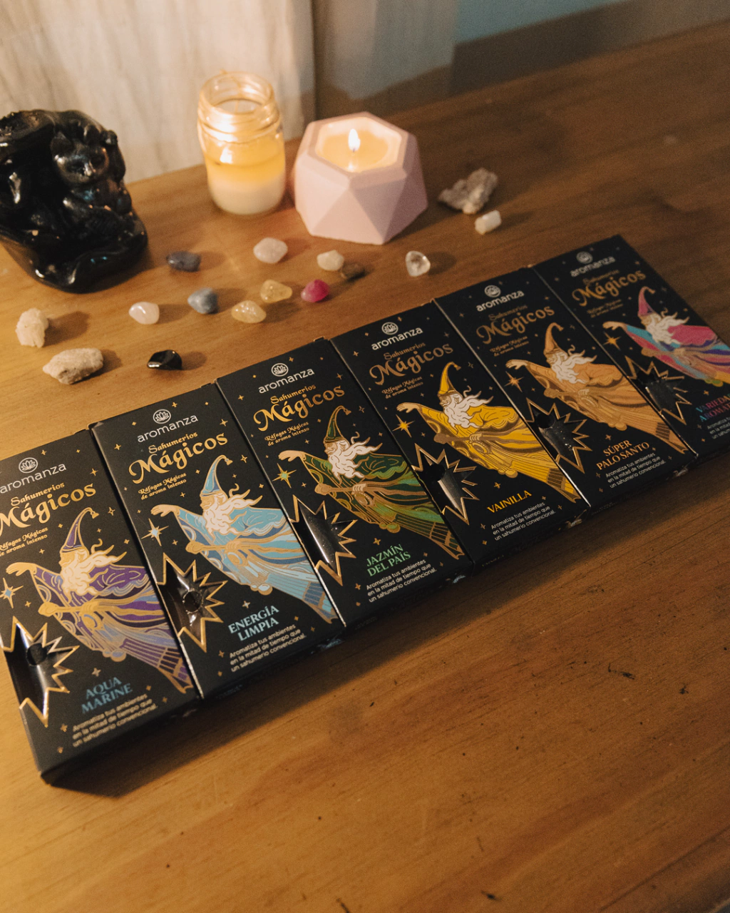 Cajas de incienso "Magicos" con velas y piedras sobre mesa de madera.