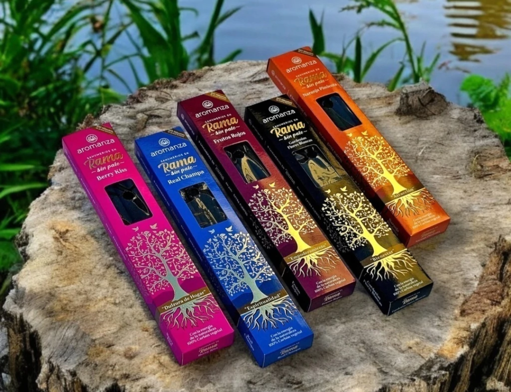 Cinco cajas de incienso de colores colocadas sobre un tocón de árbol cerca del agua. Cada caja tiene un diseño de árbol.