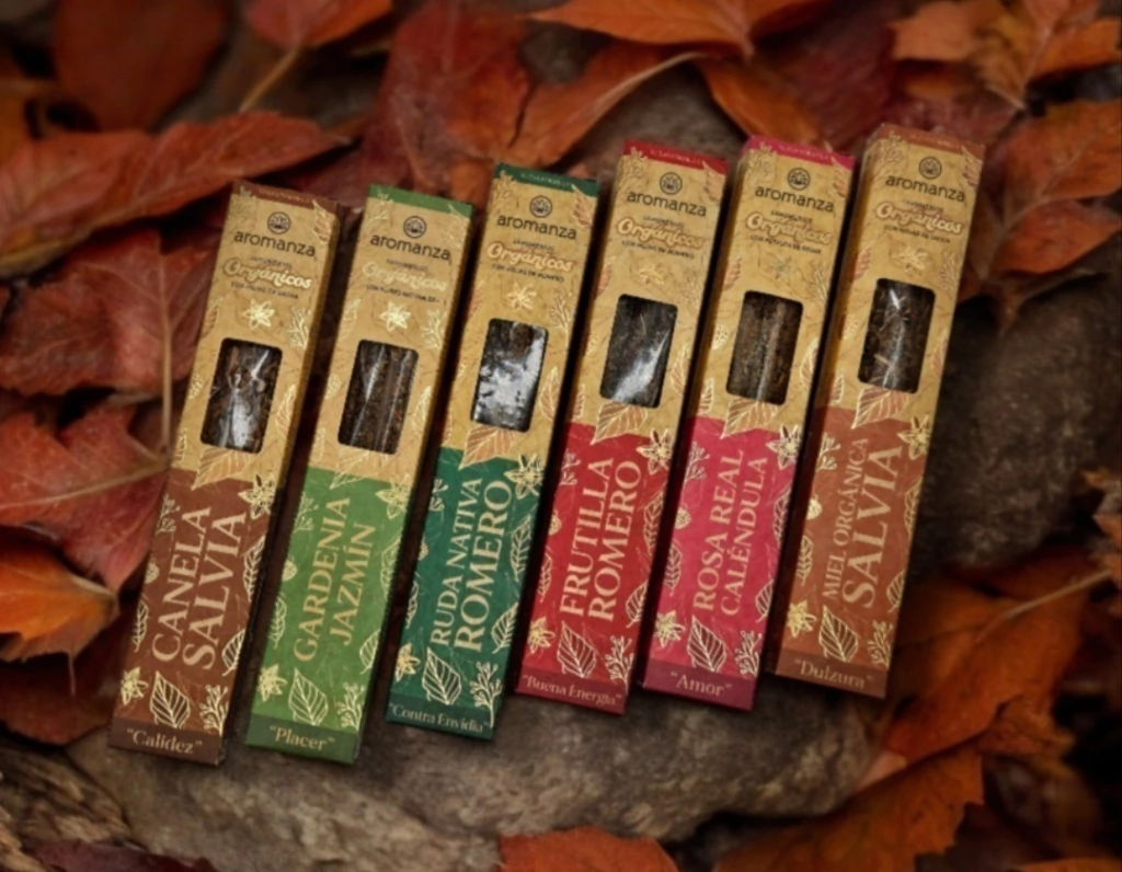Seis cajas de barritas de incienso, de diferentes colores y aromas, sobre un lecho de hojas otoñales y rocas.