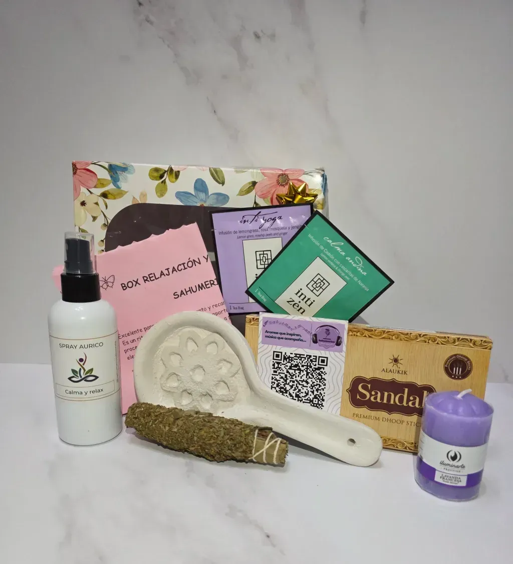 Una caja de regalo con artículos espirituales: botella de spray, manojo de salvia, incienso, vela y soporte de cerámica.