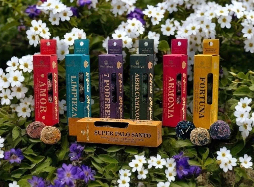Cajas de incienso surtidas etiquetadas como "Amor", "Limpieza", "7 Poderes", etc., con fondo de palo santo y flores.