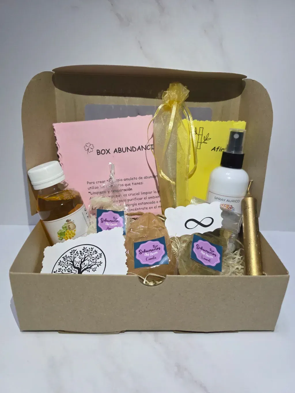 Una caja de cartón llena de artículos de cuidado personal: aerosoles, hierbas, un frasco y tarjetas rosas y amarillas.