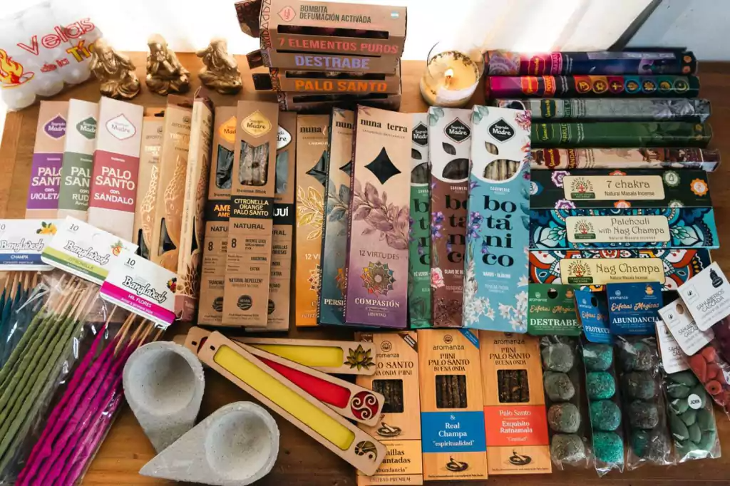 Colección de barritas de incienso, libros, velas y piedras sobre mesa de madera, varios colores y embalajes.