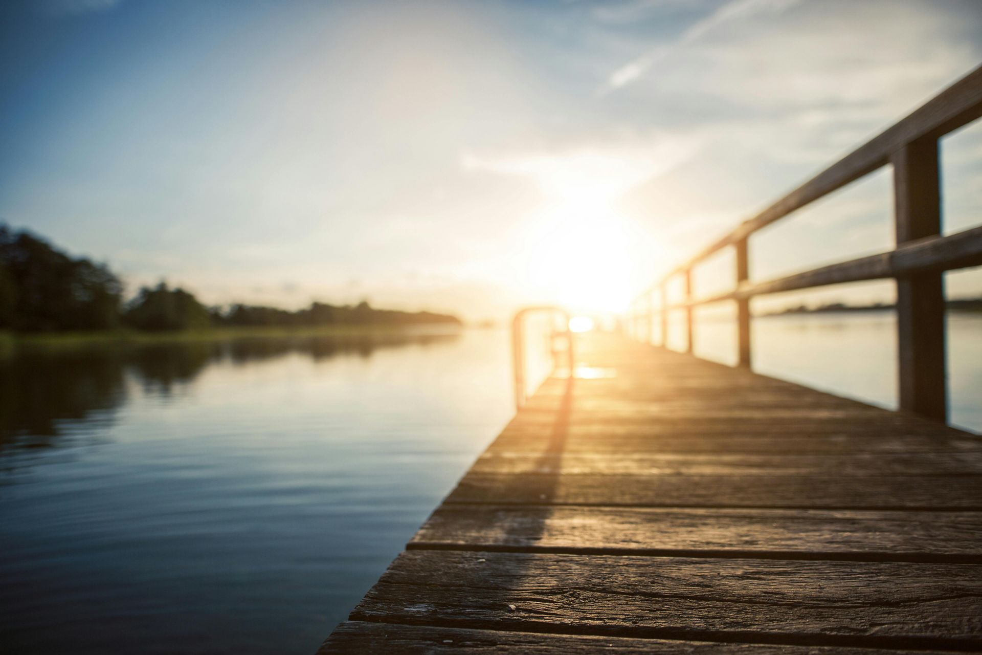 A wooden pier leading into a lake at sunset.