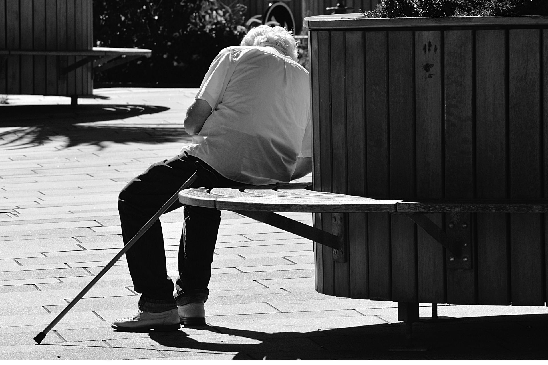 A man with a cane is sitting on a bench.