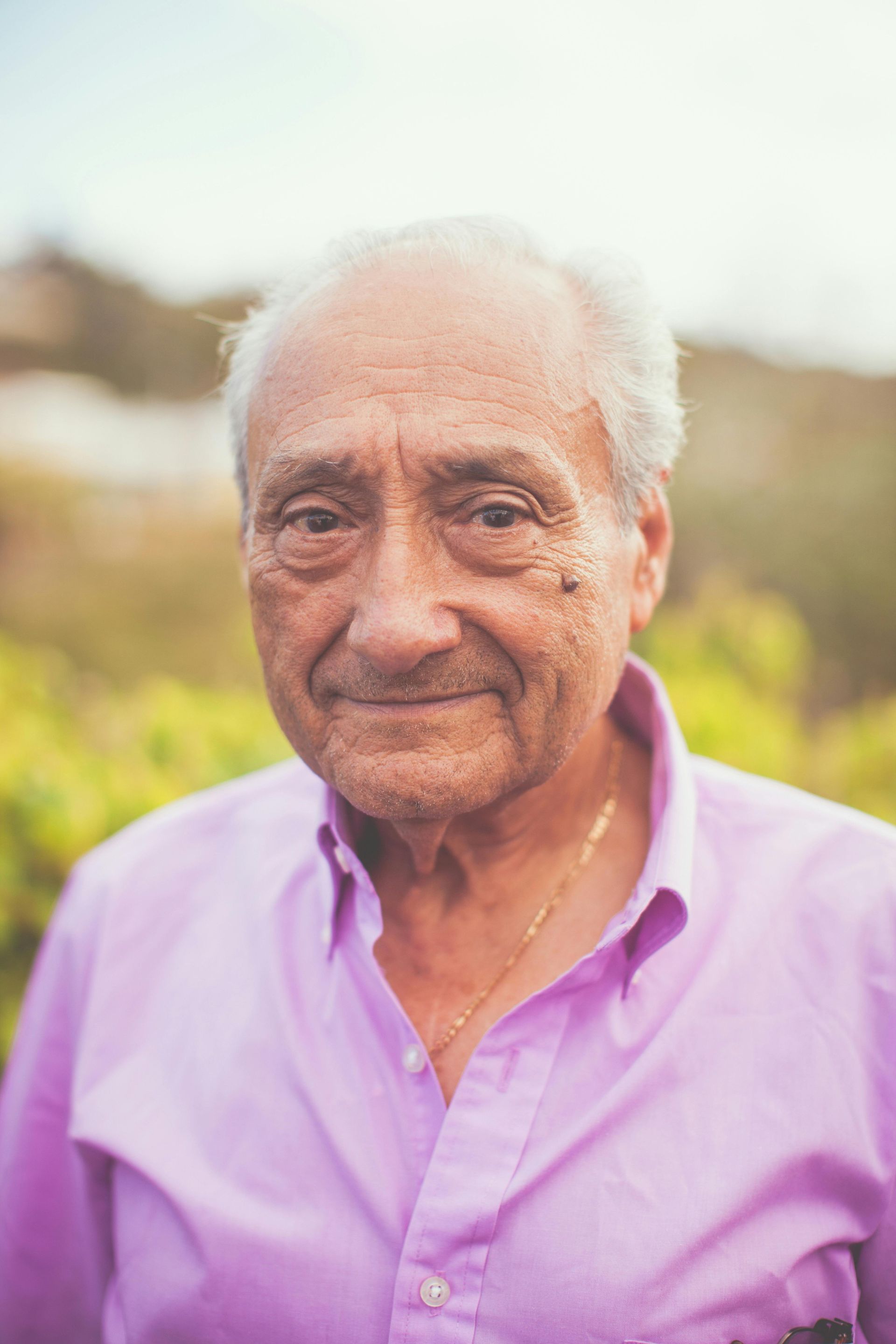 The man is wearing a purple shirt and smiling for the camera.