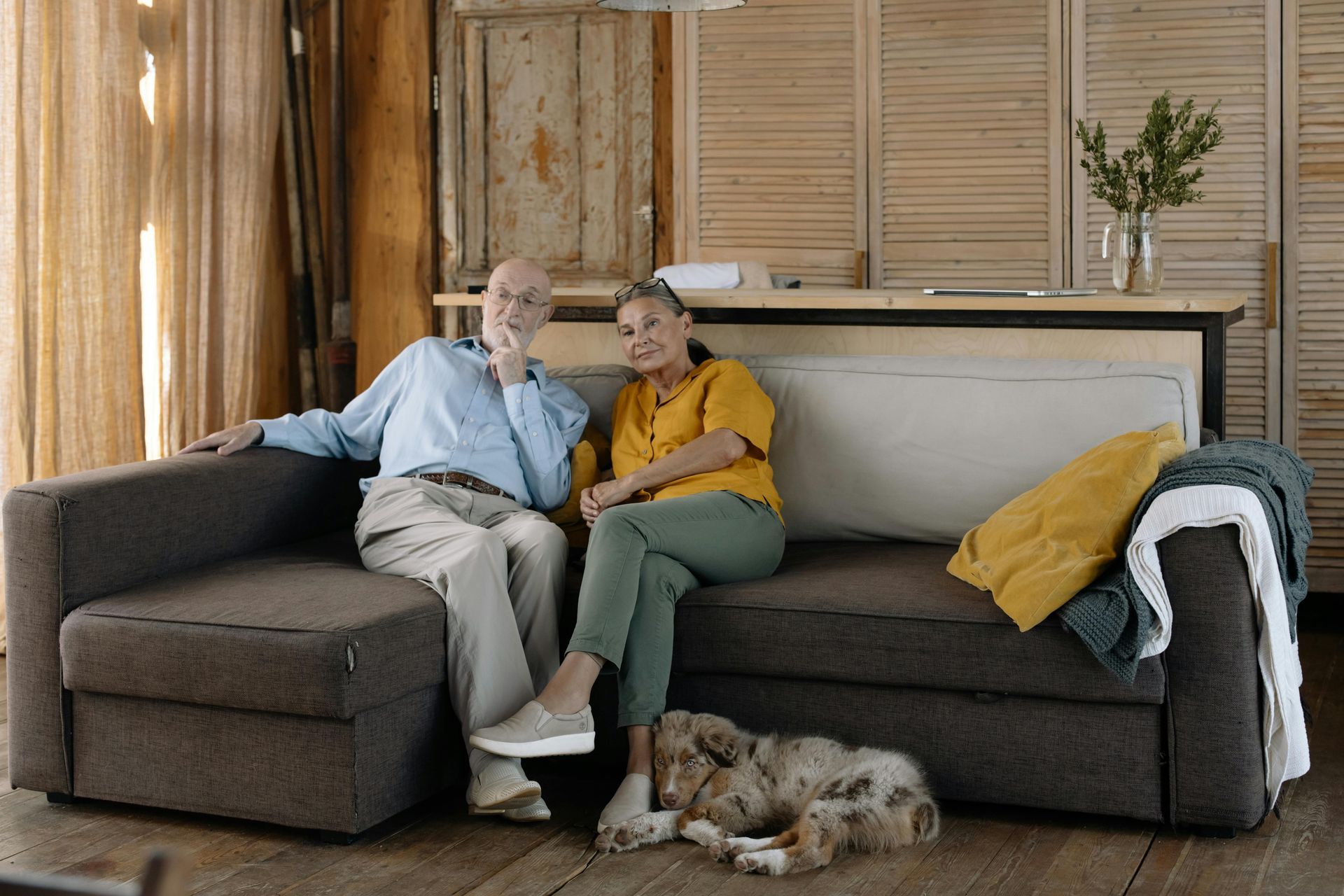 An elderly couple is sitting on a couch with a dog.