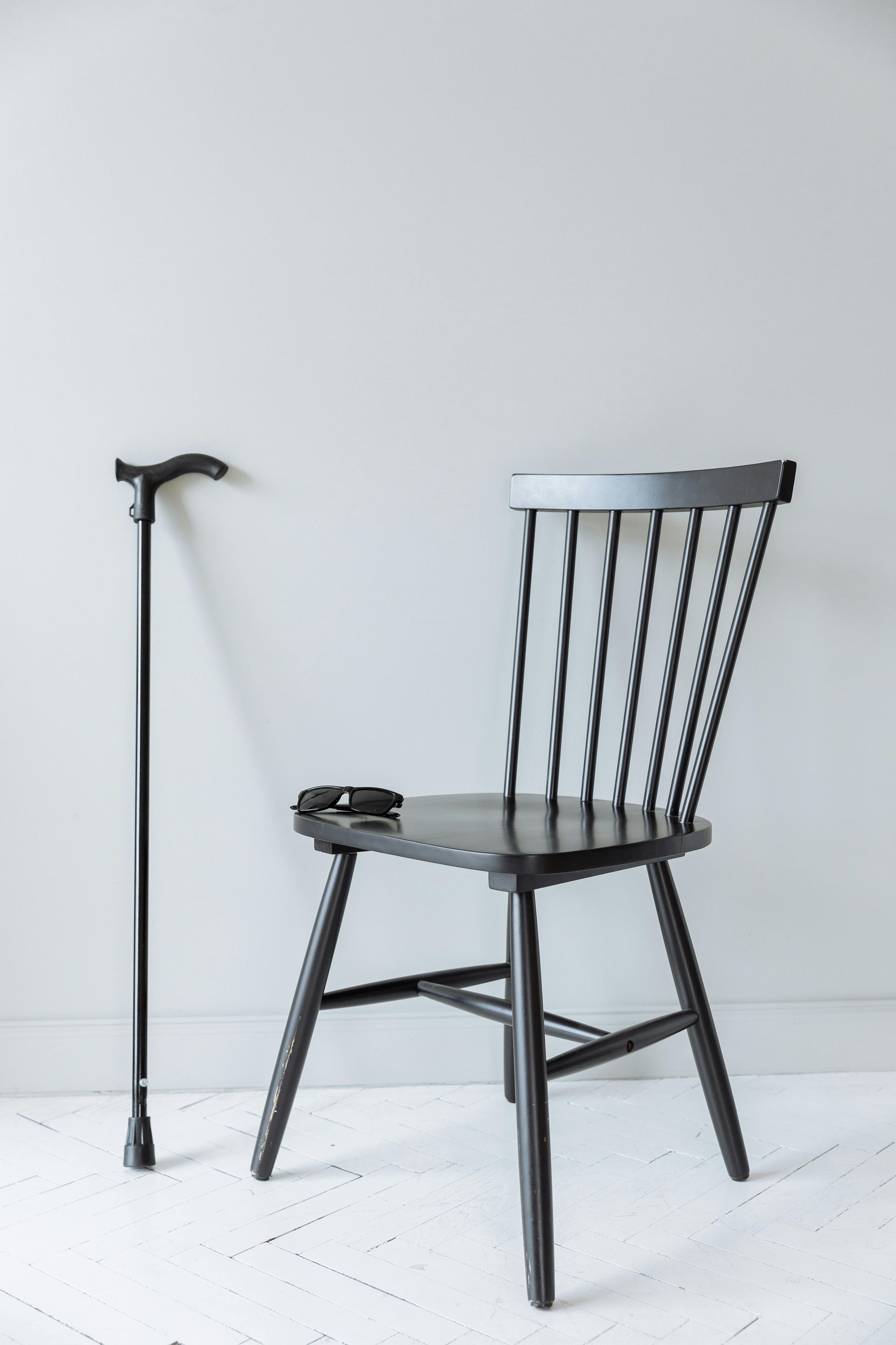 A chair and a cane are sitting next to each other on a white floor.