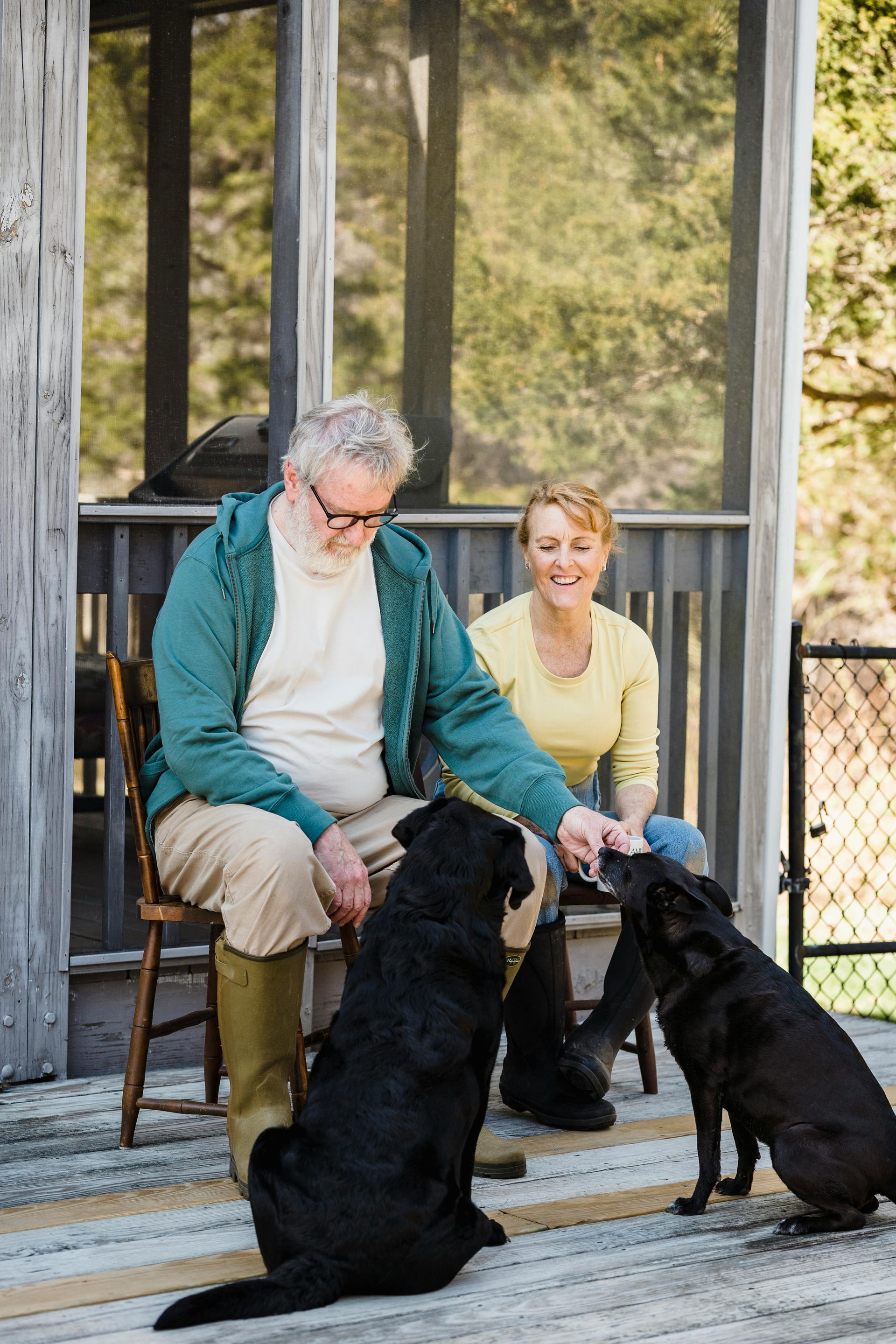 A man and a woman are sitting on a porch with their dogs.