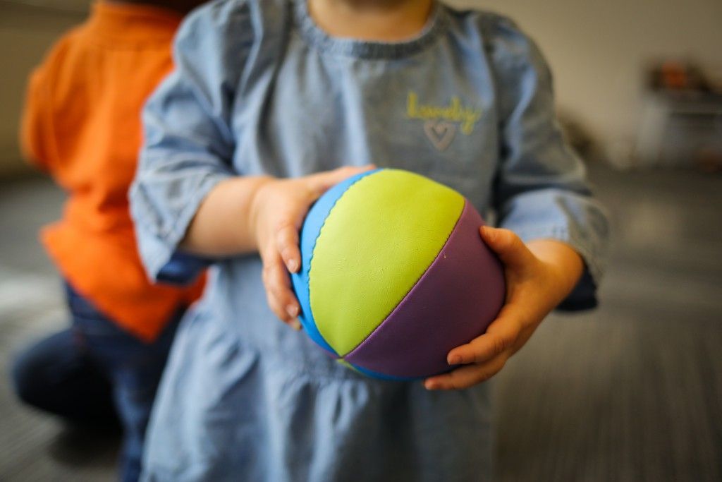 A person in a blue dress holds a colorful ball in their hands, while someone in an orange shirt stands behind them.
