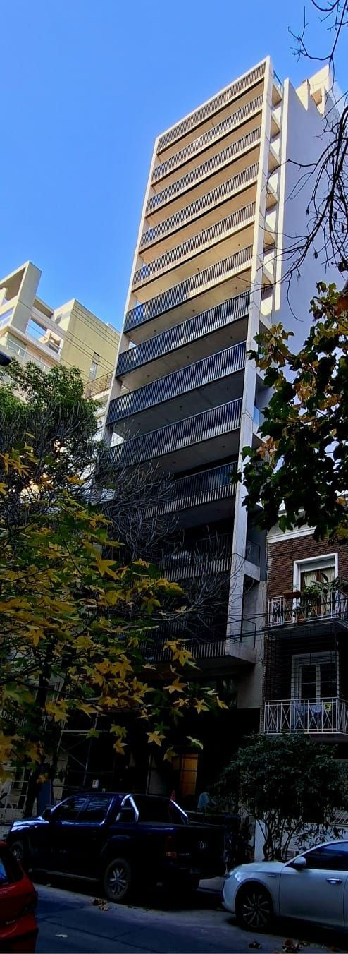 Un edificio alto está rodeado de árboles y coches en una calle de la ciudad.