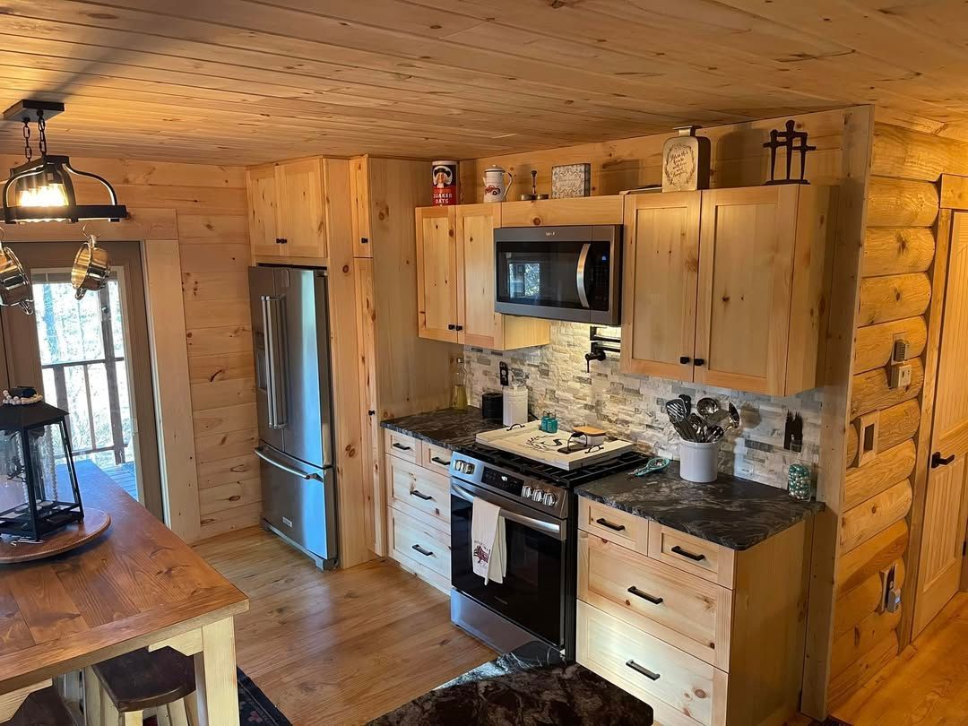 Cozy cabin kitchen with stainless steel appliances, light wood cabinets, and stone backsplash.