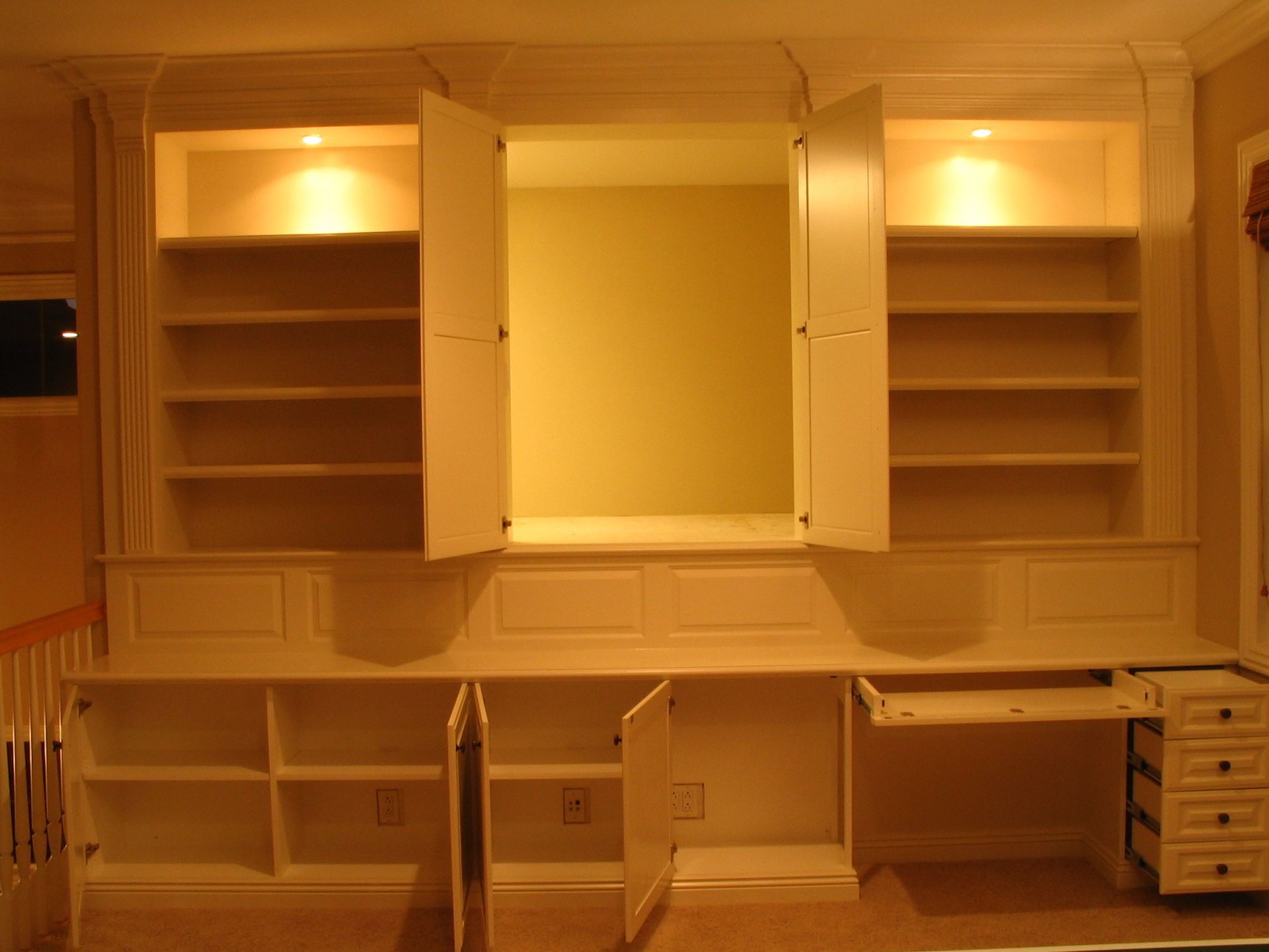 Built-in white shelving and desk with open cabinets, illuminated with recessed lighting.
