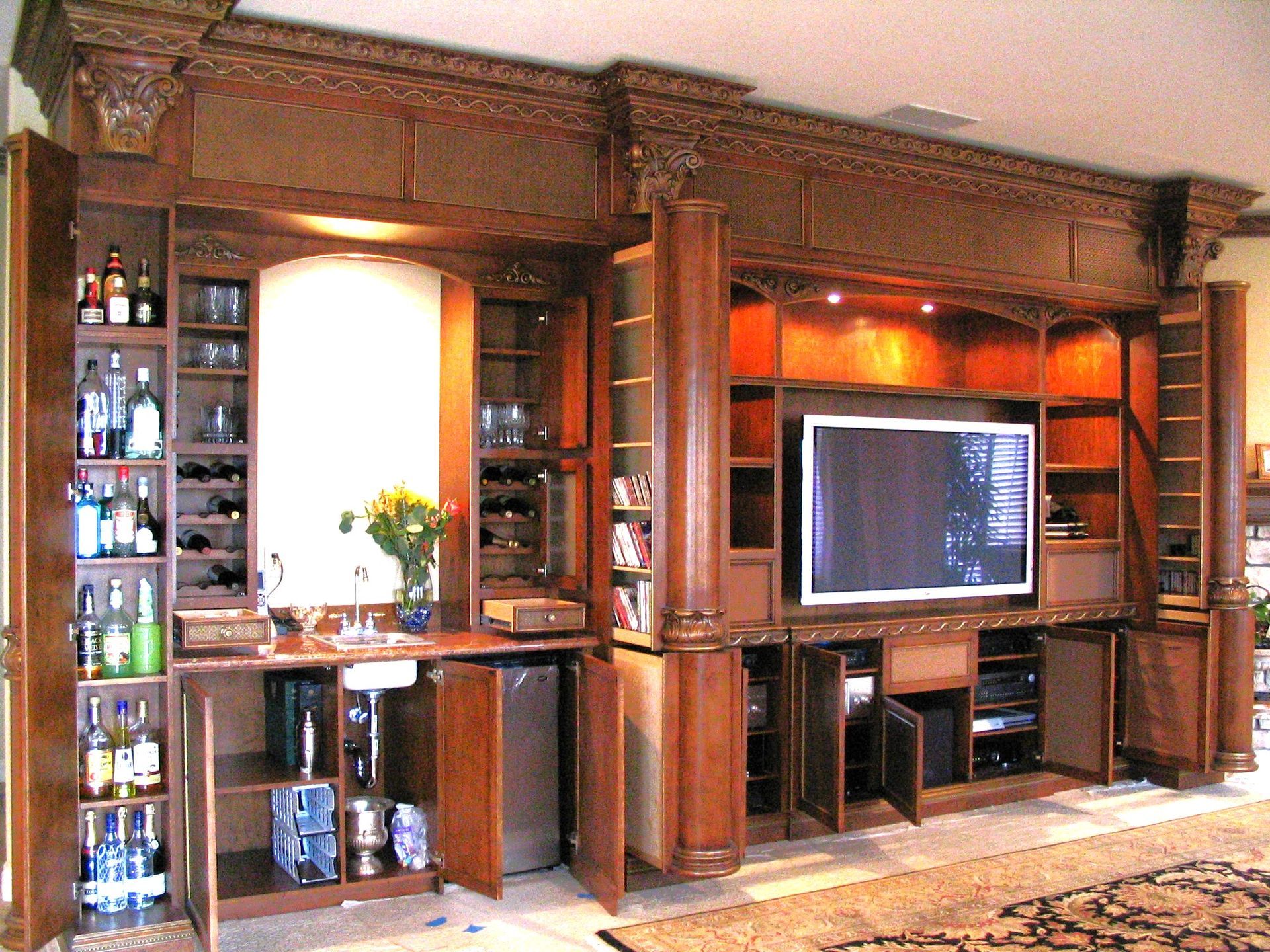 Built-in wooden entertainment center with open cabinets, bar area, TV, and decorative crown molding.