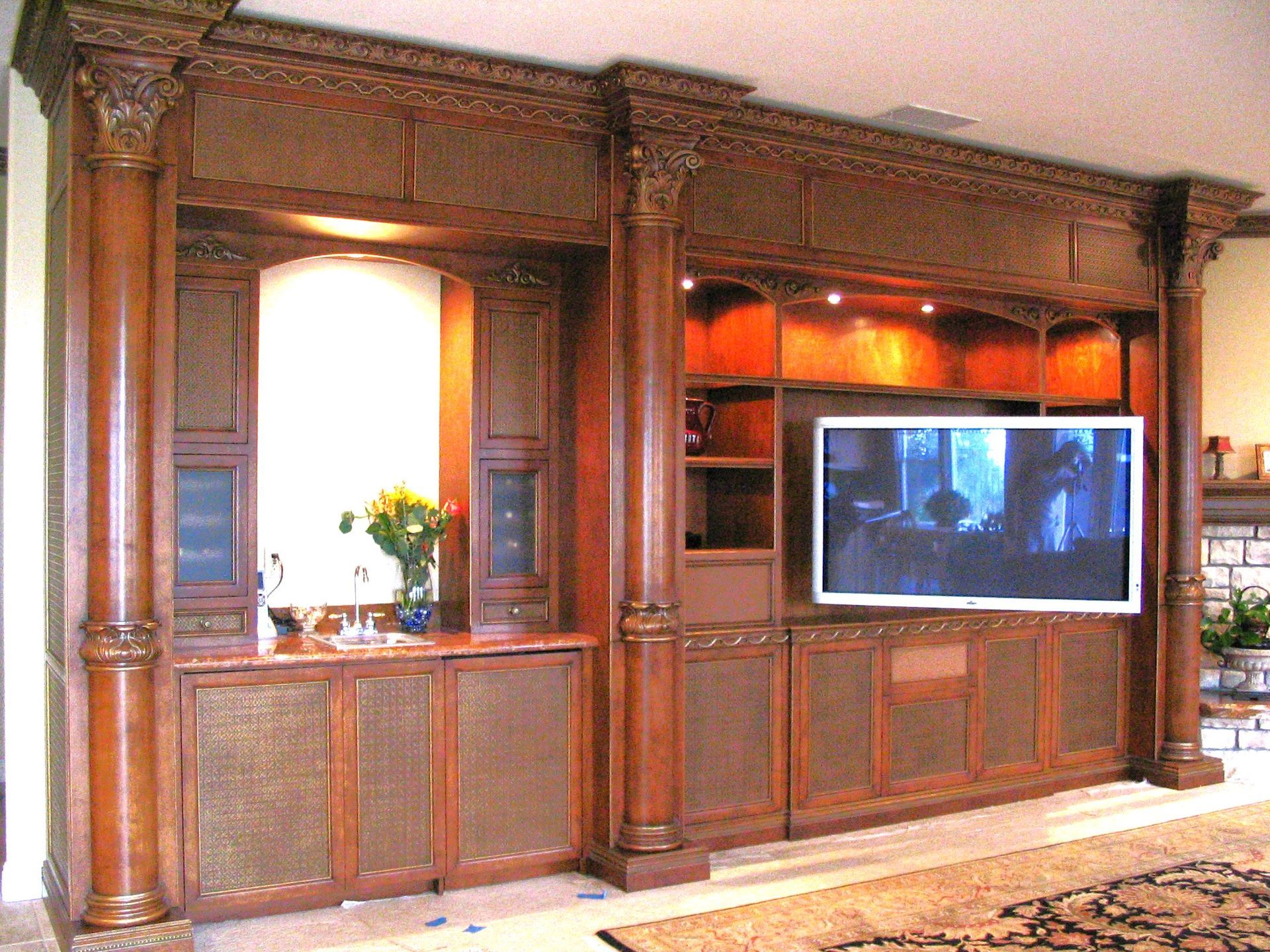 Built-in wooden entertainment center with TV, cabinetry, and columns, in a living room.