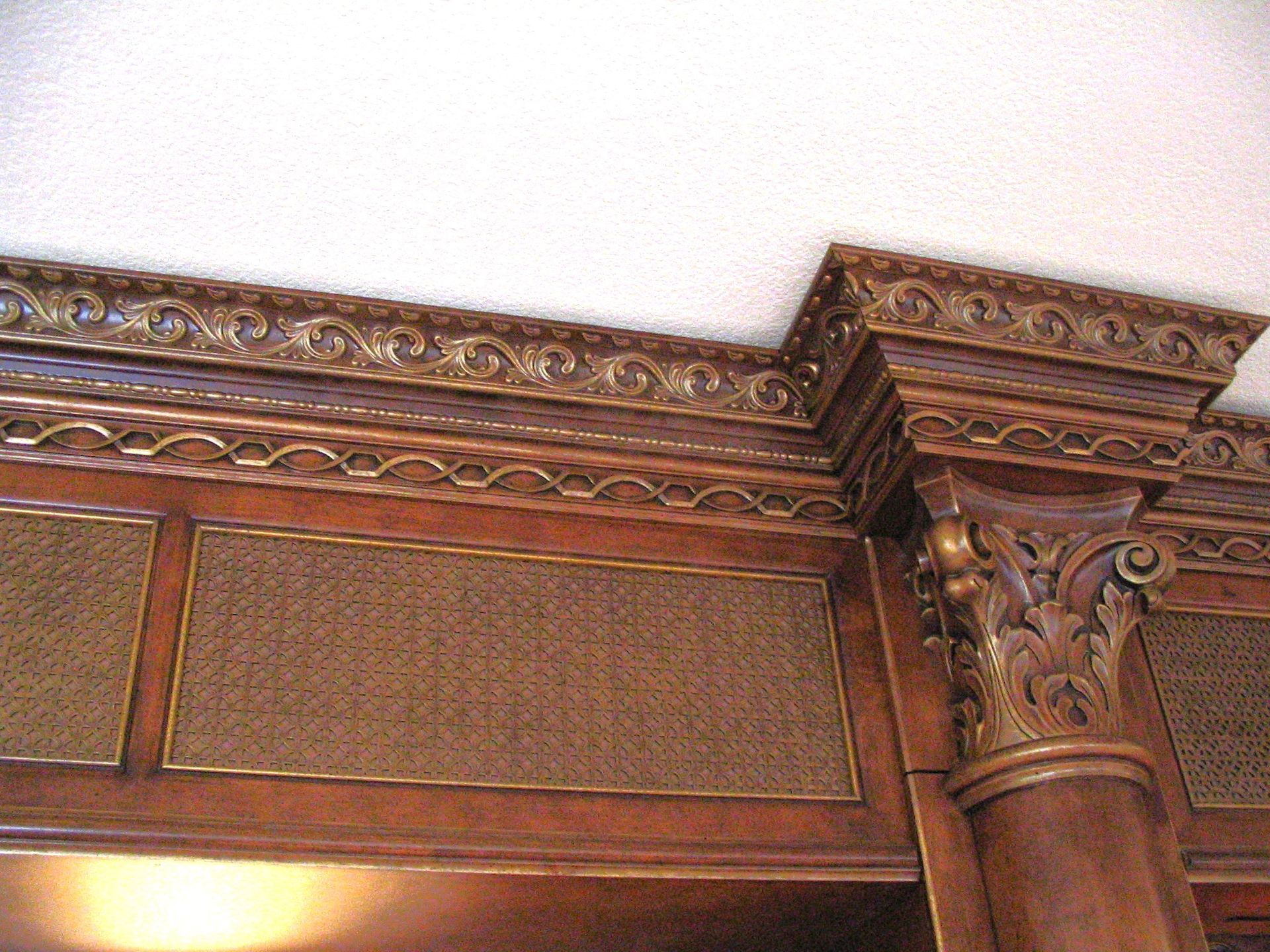 Ornate wooden cabinet detail with decorative molding and a column topped with a carved capital.