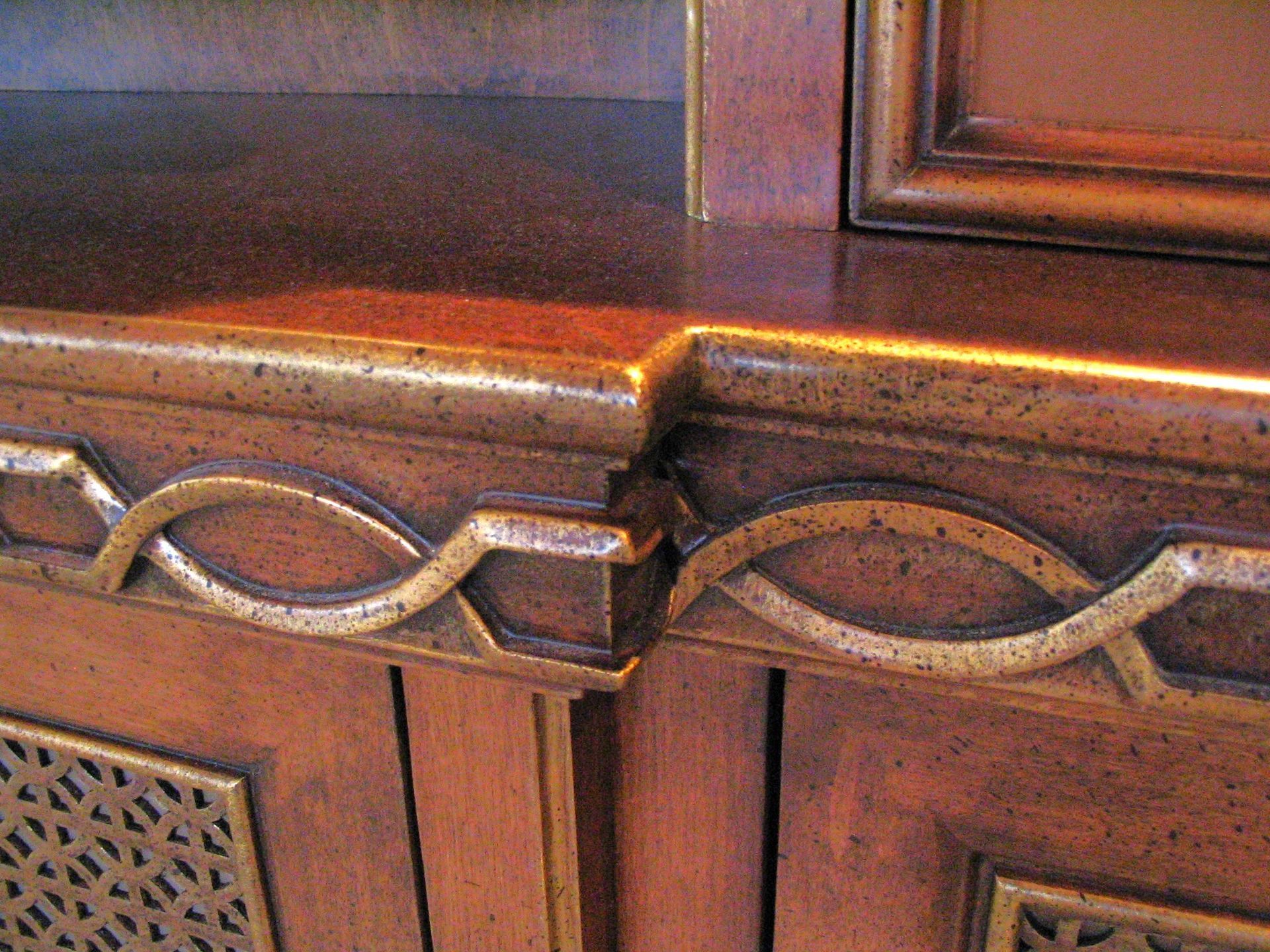 Close-up of a wooden cabinet with ornate gold-colored trim and a decorative curved pattern.