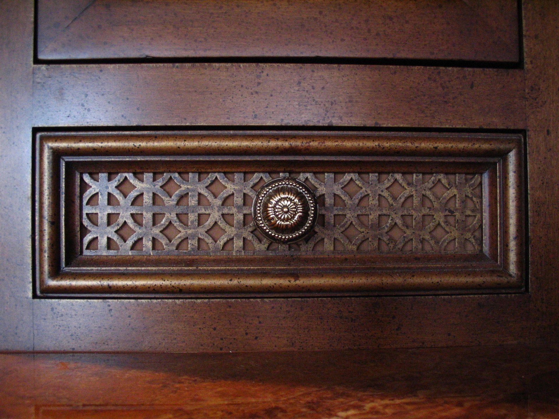 Close-up of a wooden cabinet detail with a decorative rectangular vent and a circular knob.