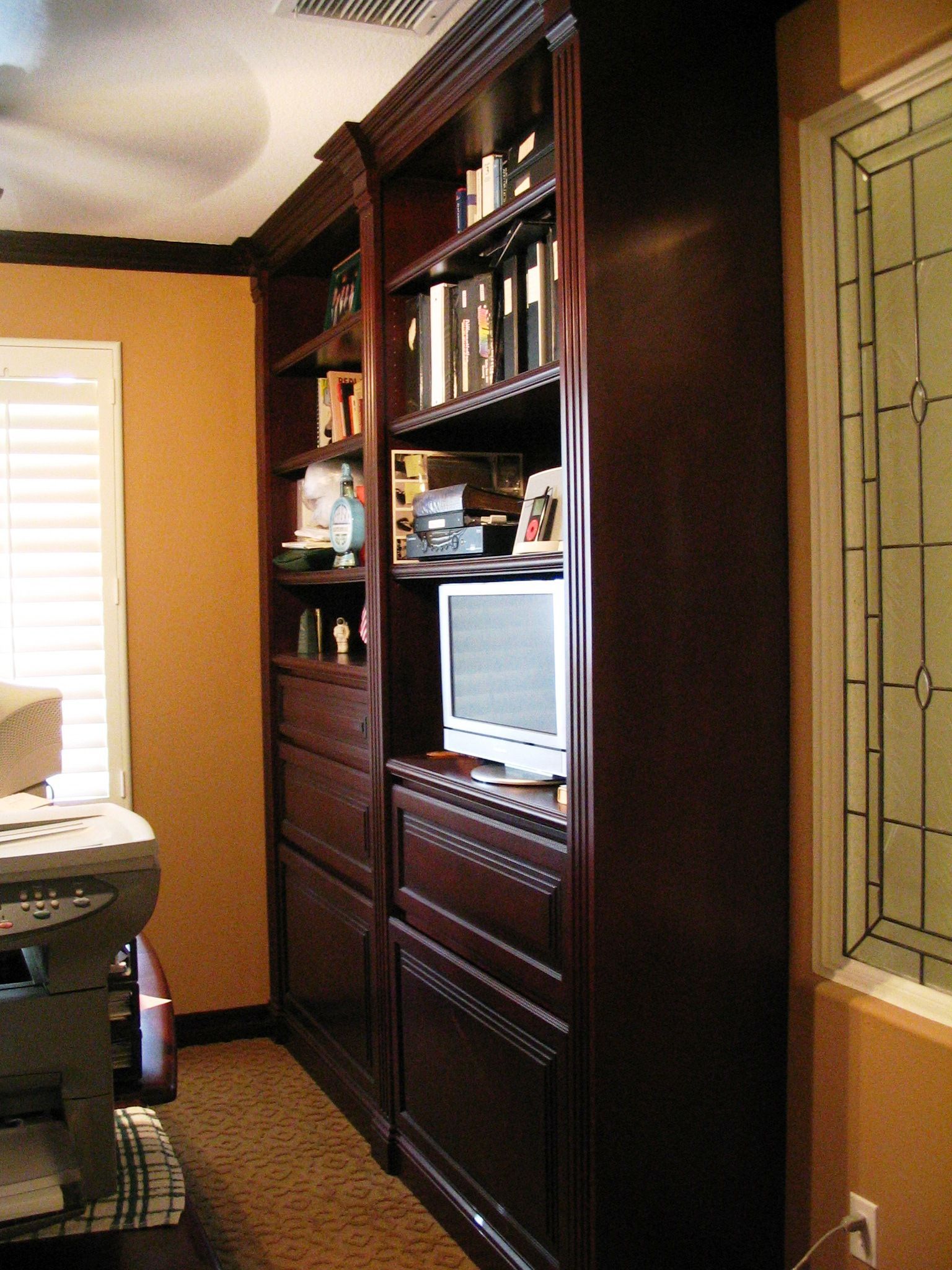Dark wood built-in bookshelves against an orange wall. Window with decorative glass to the right.