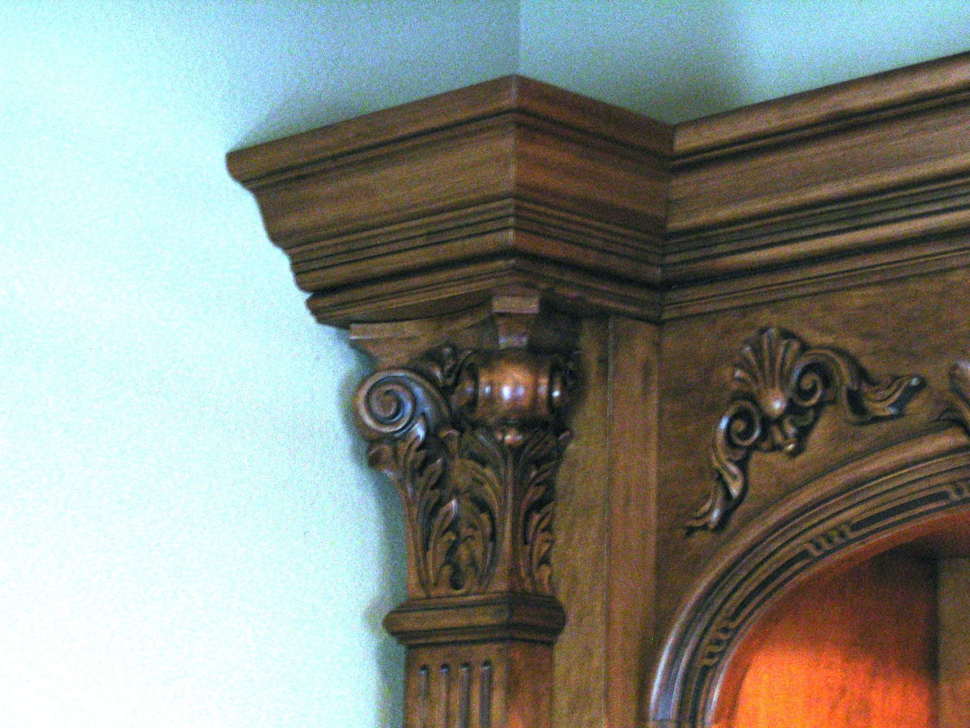 Corner of ornate, dark wood built-in shelving with carved details and molding against a pale green wall.