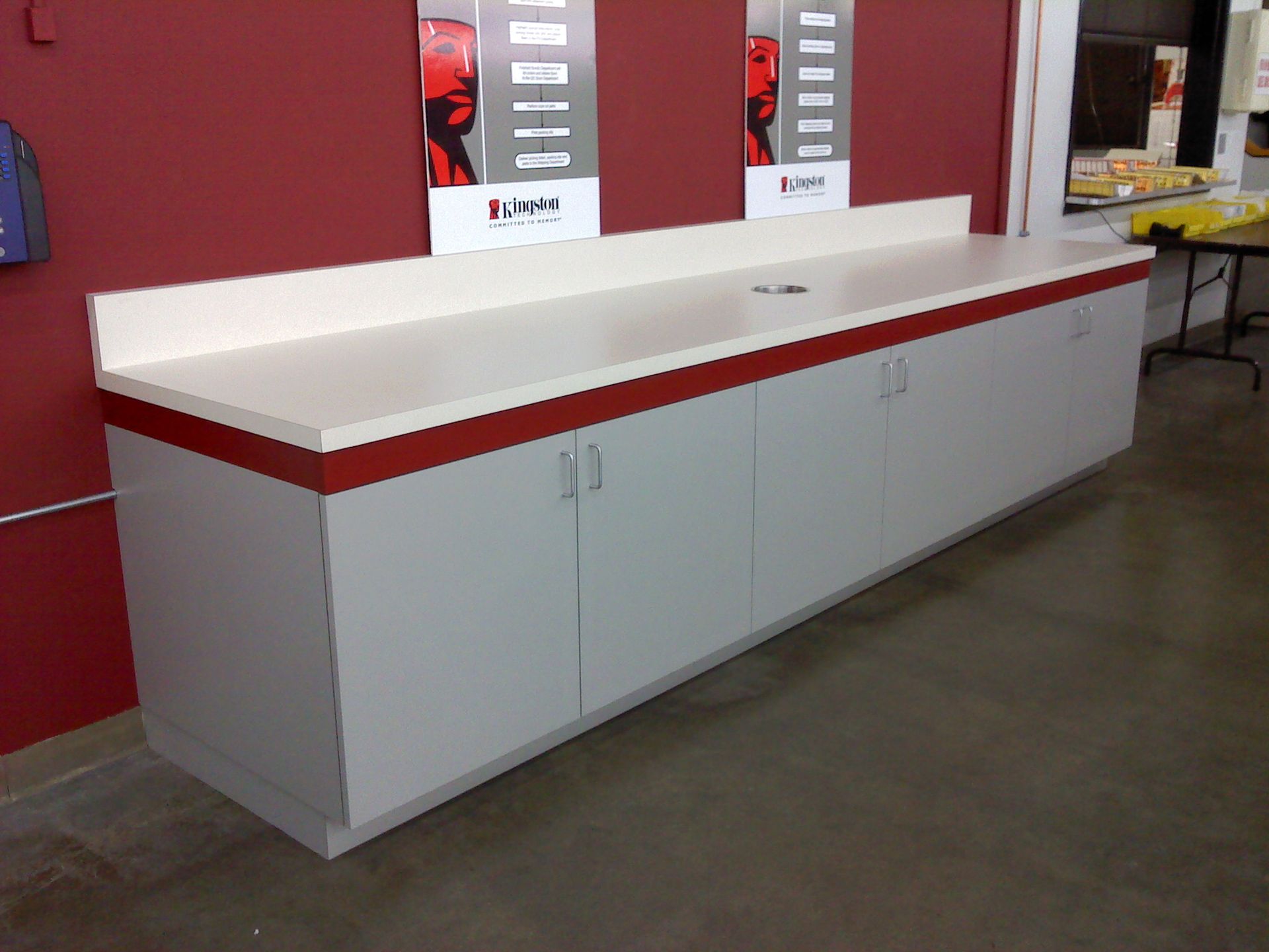 Long white counter with red trim and cabinets below against a red wall.