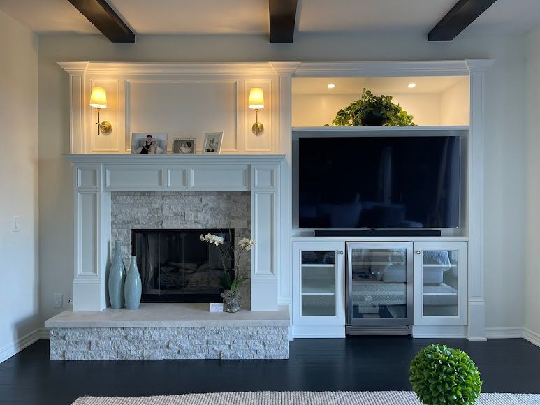 Built-in white media center with TV, fireplace, and shelves with wood backing; a person on screen.