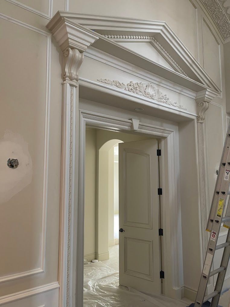 Architectural doorway with decorative molding and open door to hallway. Light color scheme, ladder visible.