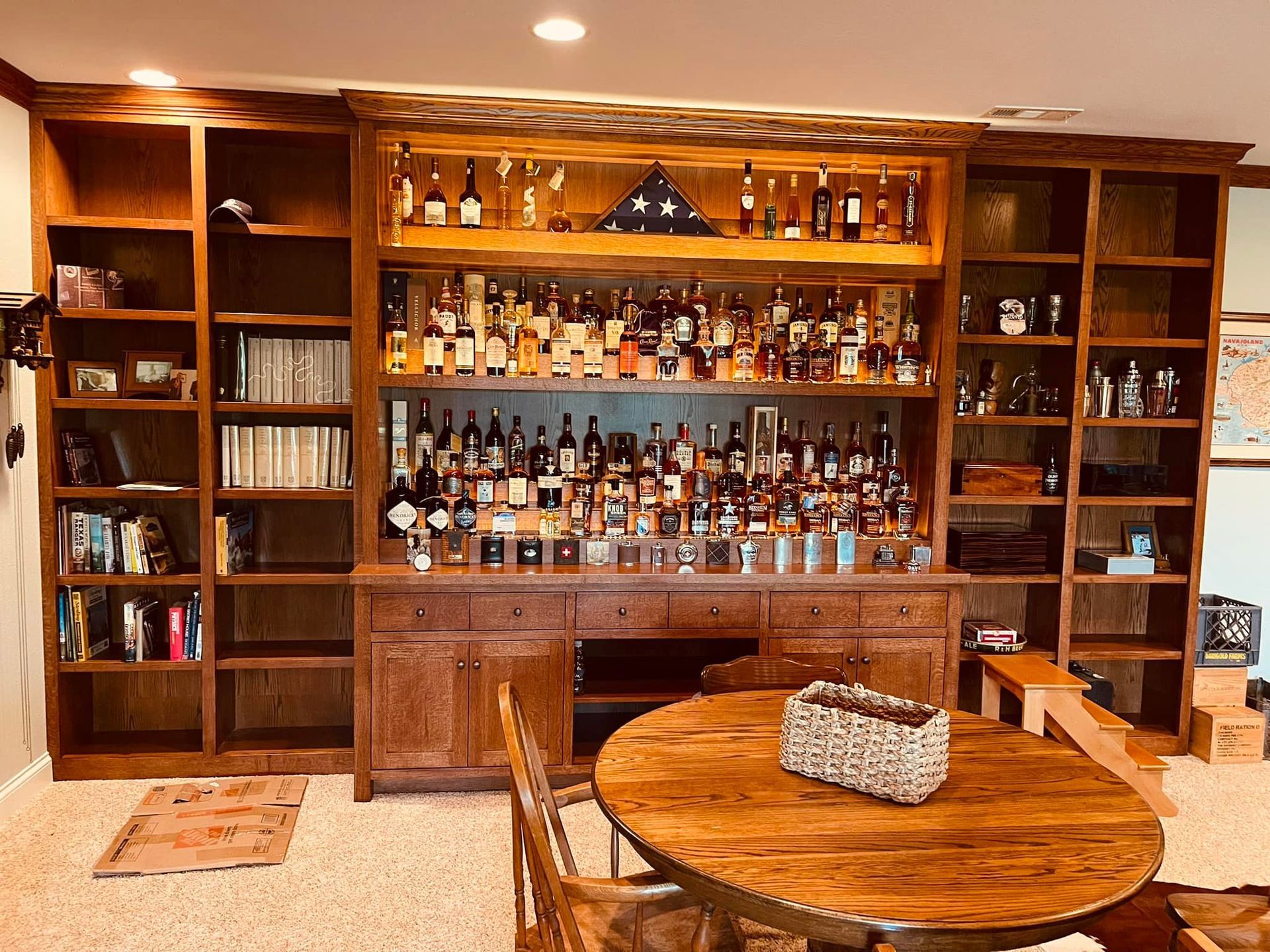 Wooden home bar with many liquor bottles, shelves, and a round table.