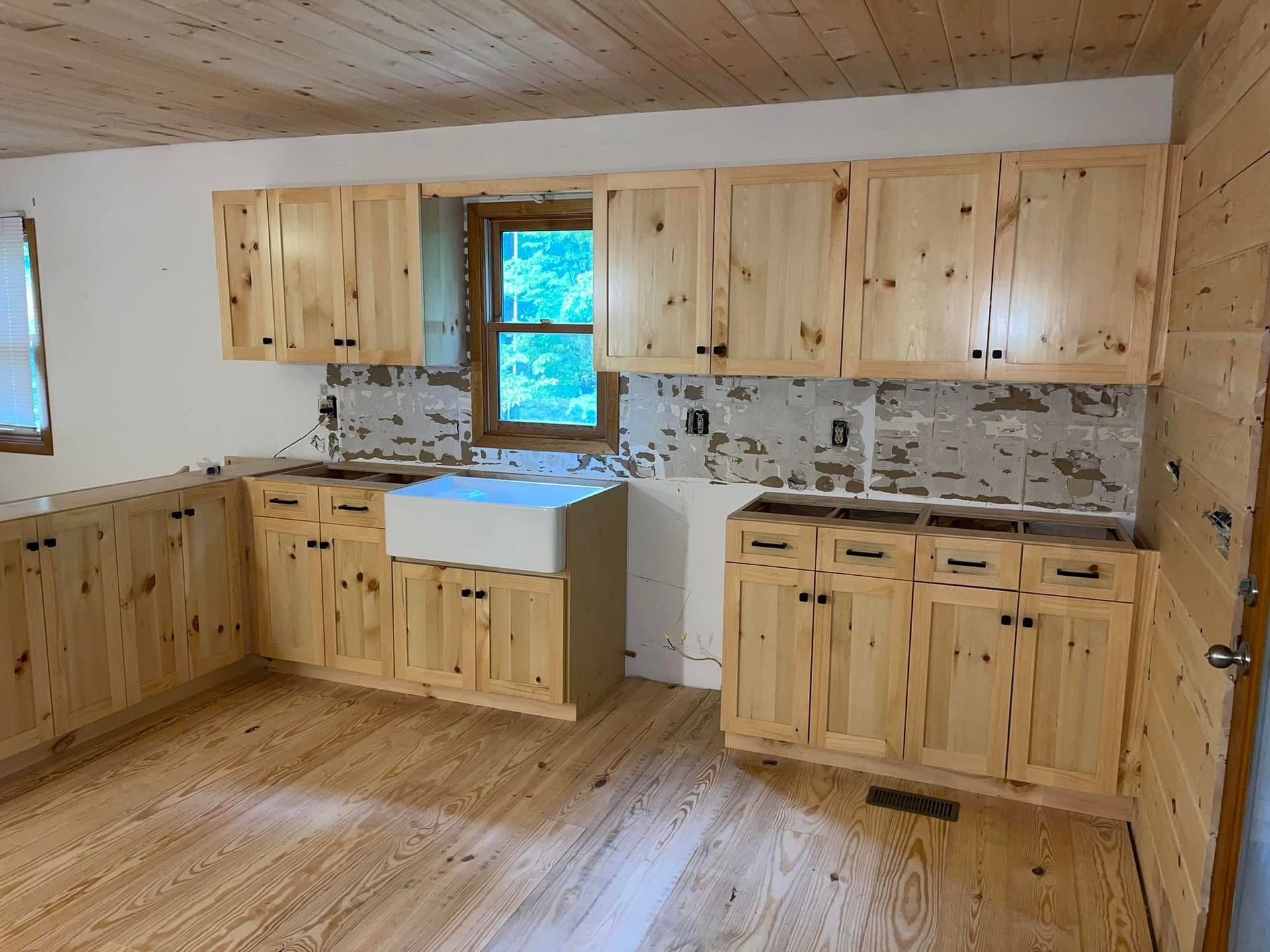 Kitchen with light wood cabinets, flooring and ceiling. A white farmhouse sink is visible.